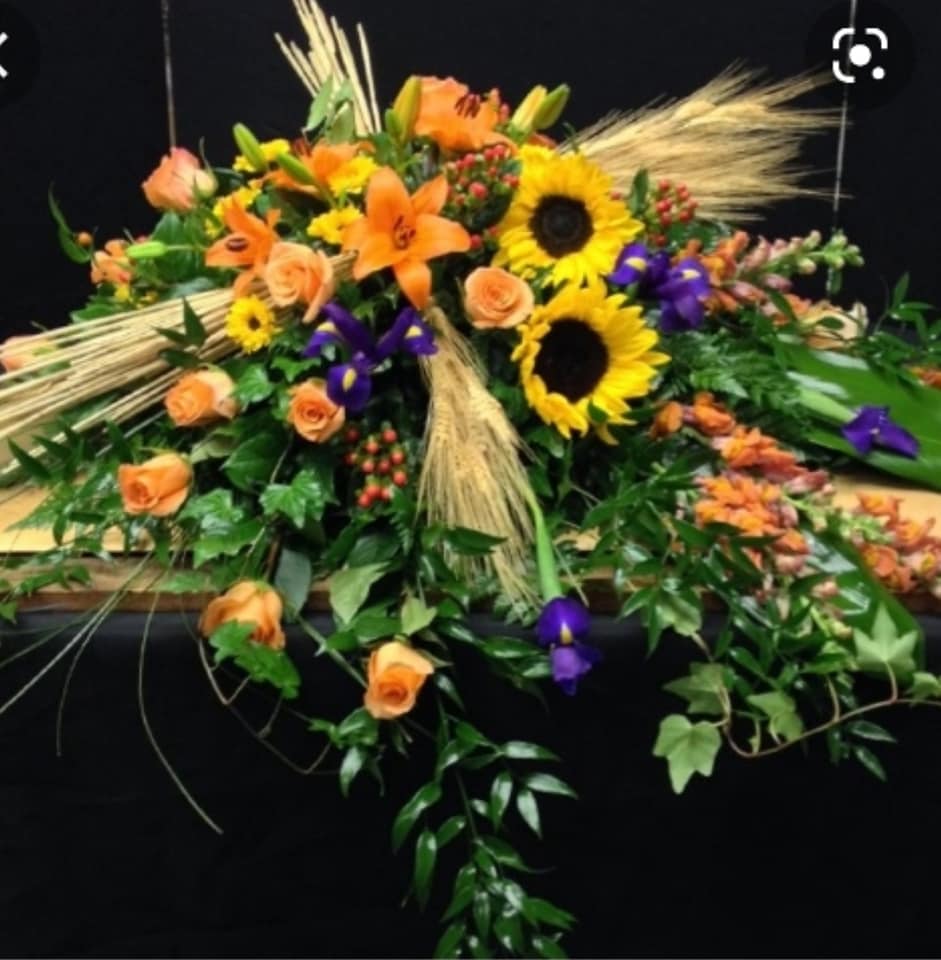 Orange roses and sunflowers arranged with purple flowers and wheat accents