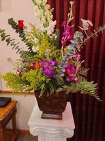 Tall mixed floral arrangement in a dark urn on a table