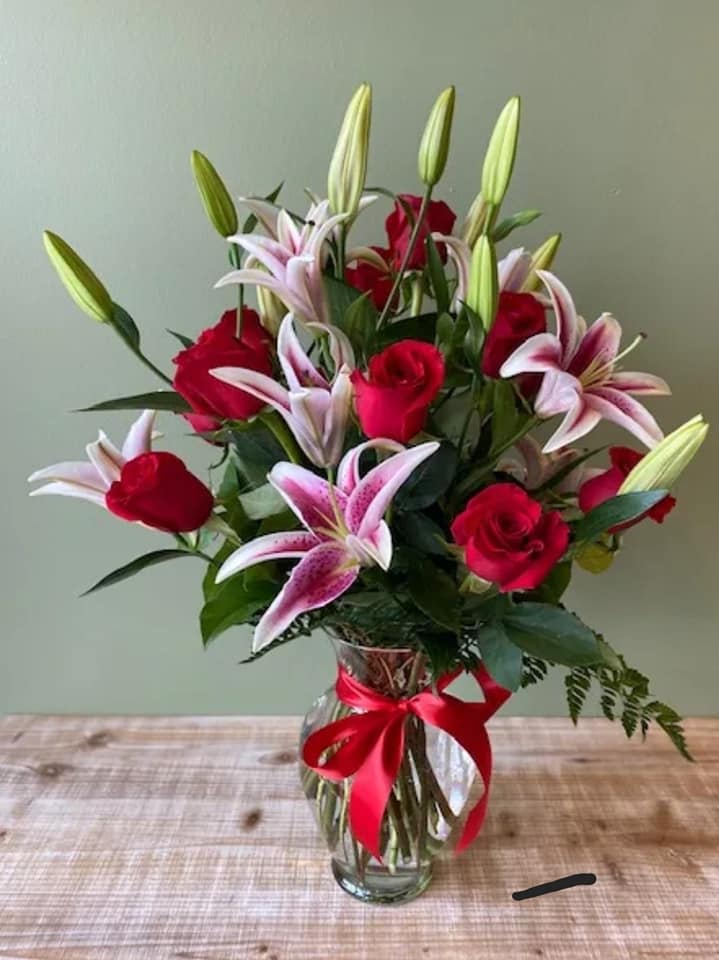 Red roses and pink lilies in a clear glass vase with a red ribbon