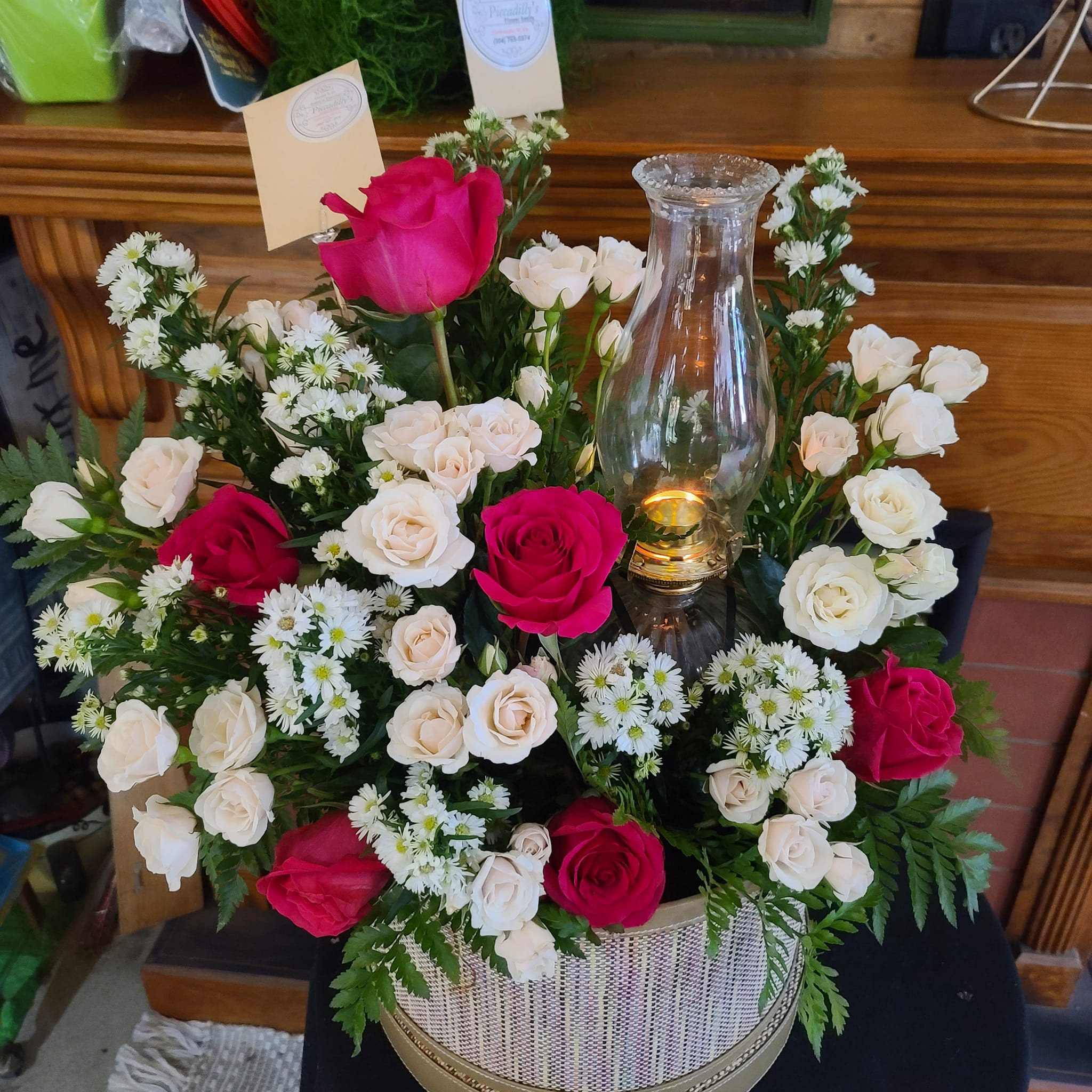 Pink and white roses arranged around a glass candle holder in a basket.