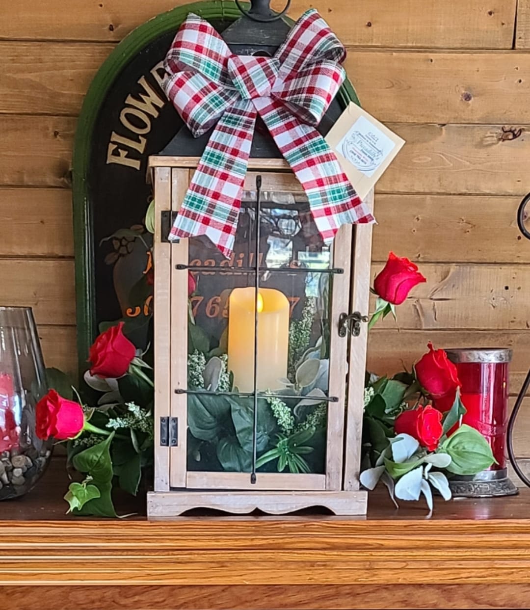 Lantern with candle, red roses, and plaid bow on a wooden shelf