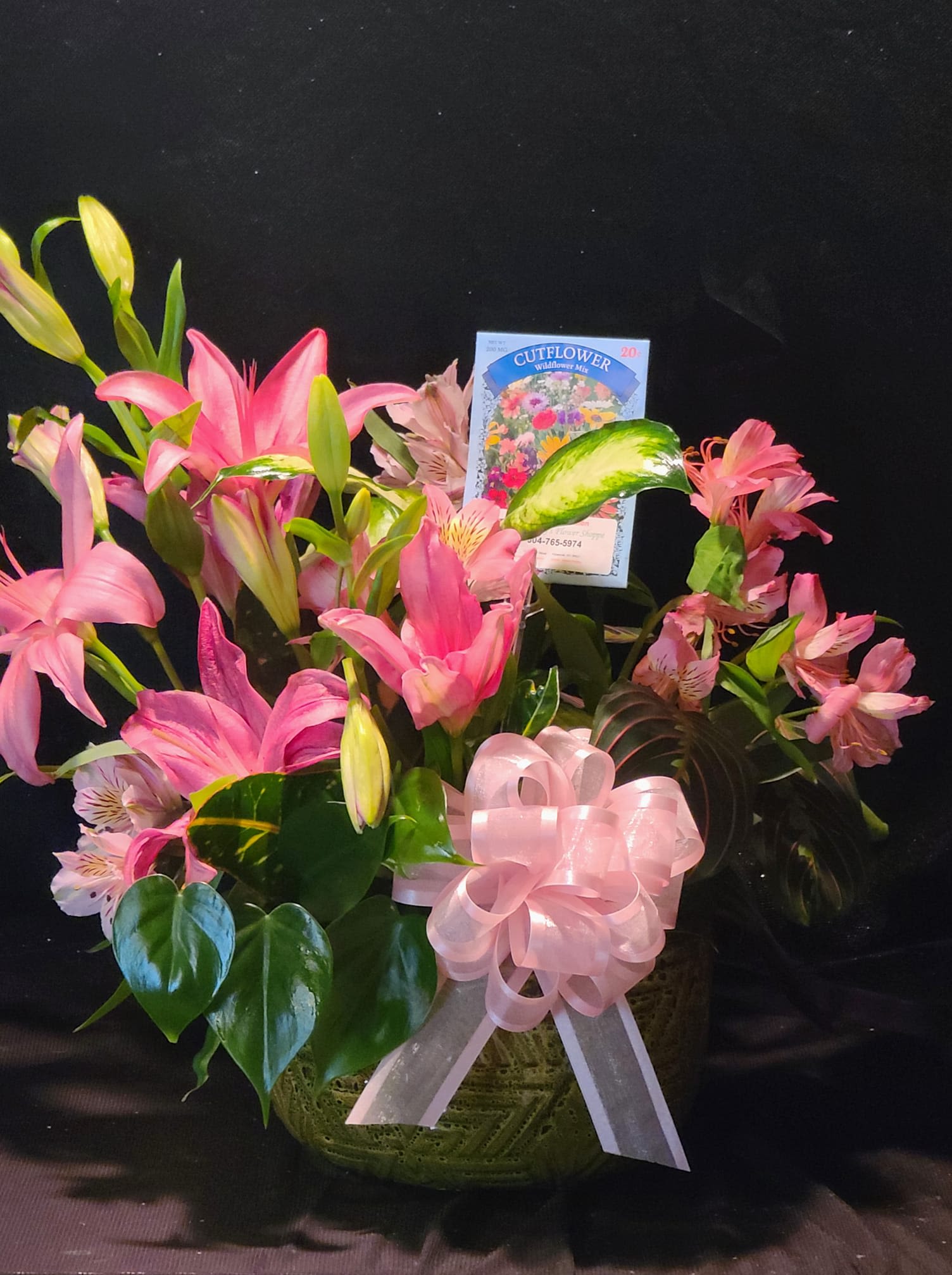Pink lilies and alstroemeria in a basket with a pink ribbon bow