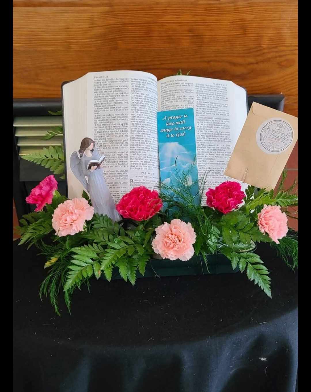 Pink carnations arranged around an open Bible with an angel figurine