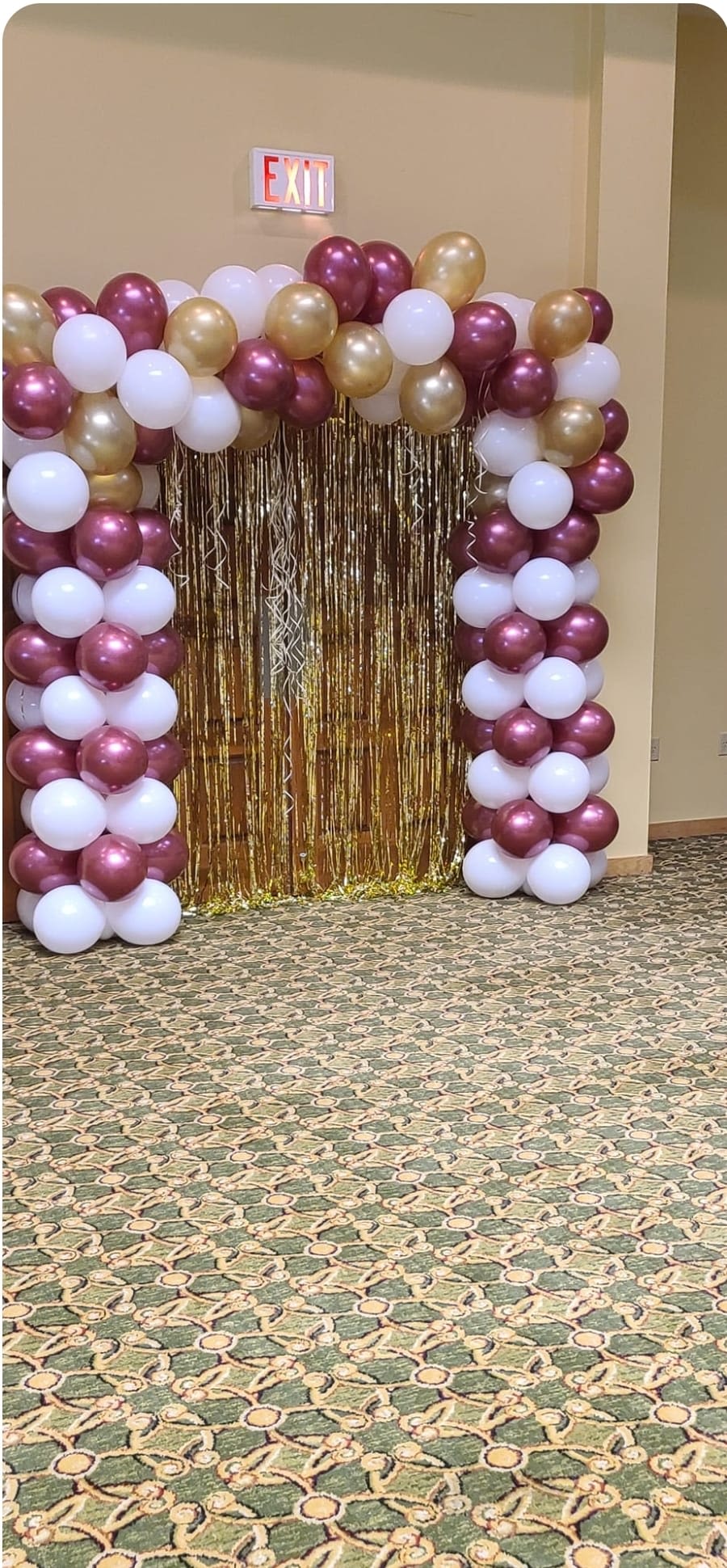 Balloon arch in burgundy, white, and gold with a metallic fringe backdrop
