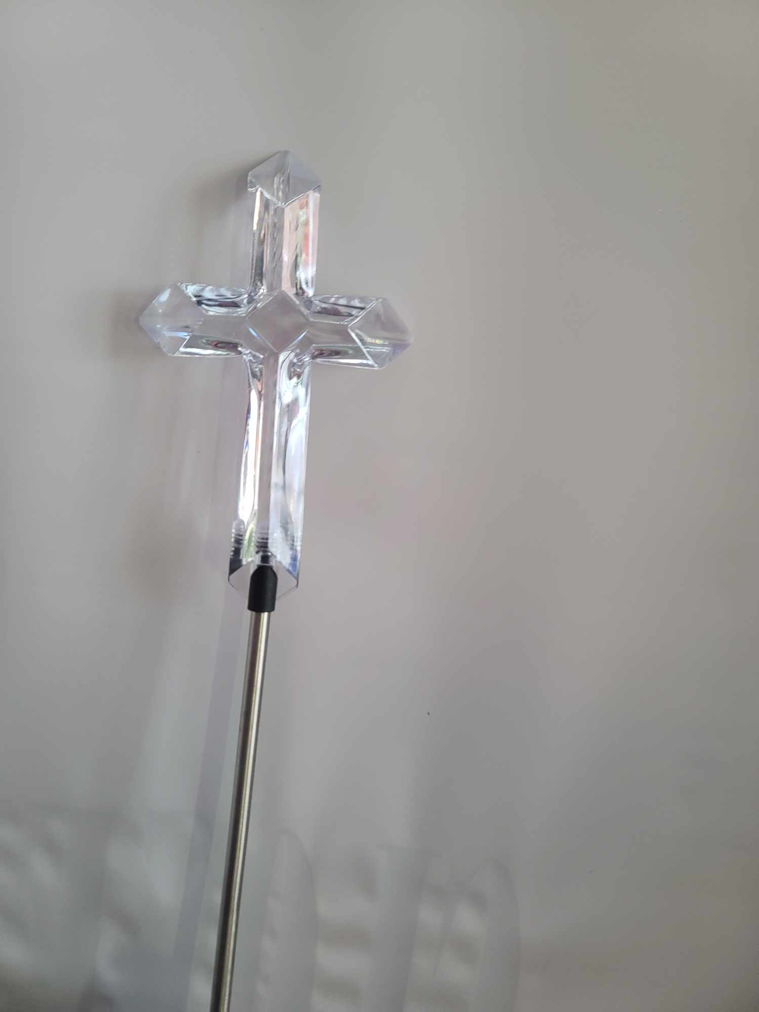 Clear crystal cross on a metal stand against a plain background