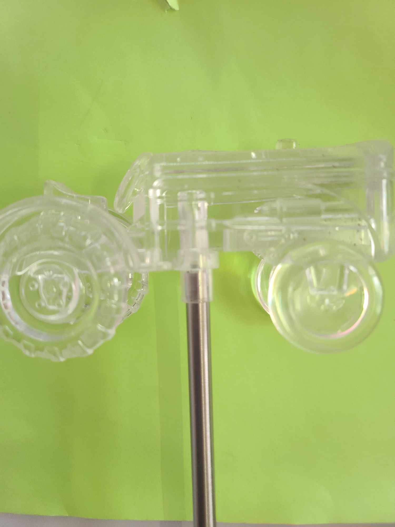Clear plastic toy car mounted on a metal rod against a green background