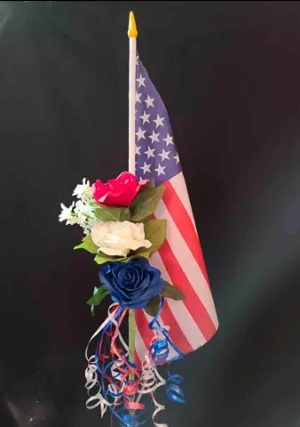 Small floral arrangement with red, white, and blue roses beside an American flag