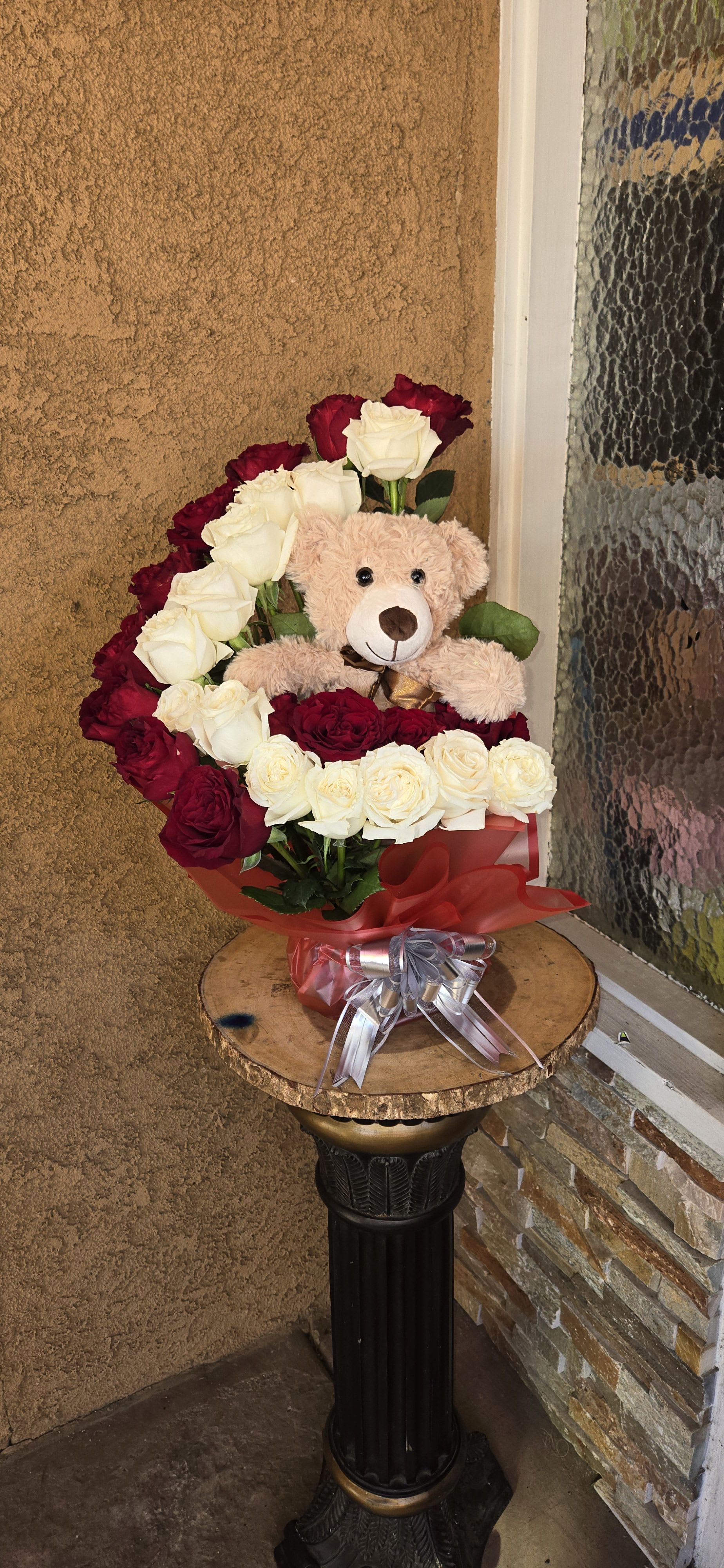 Red and white roses arranged with a teddy bear and ribbon