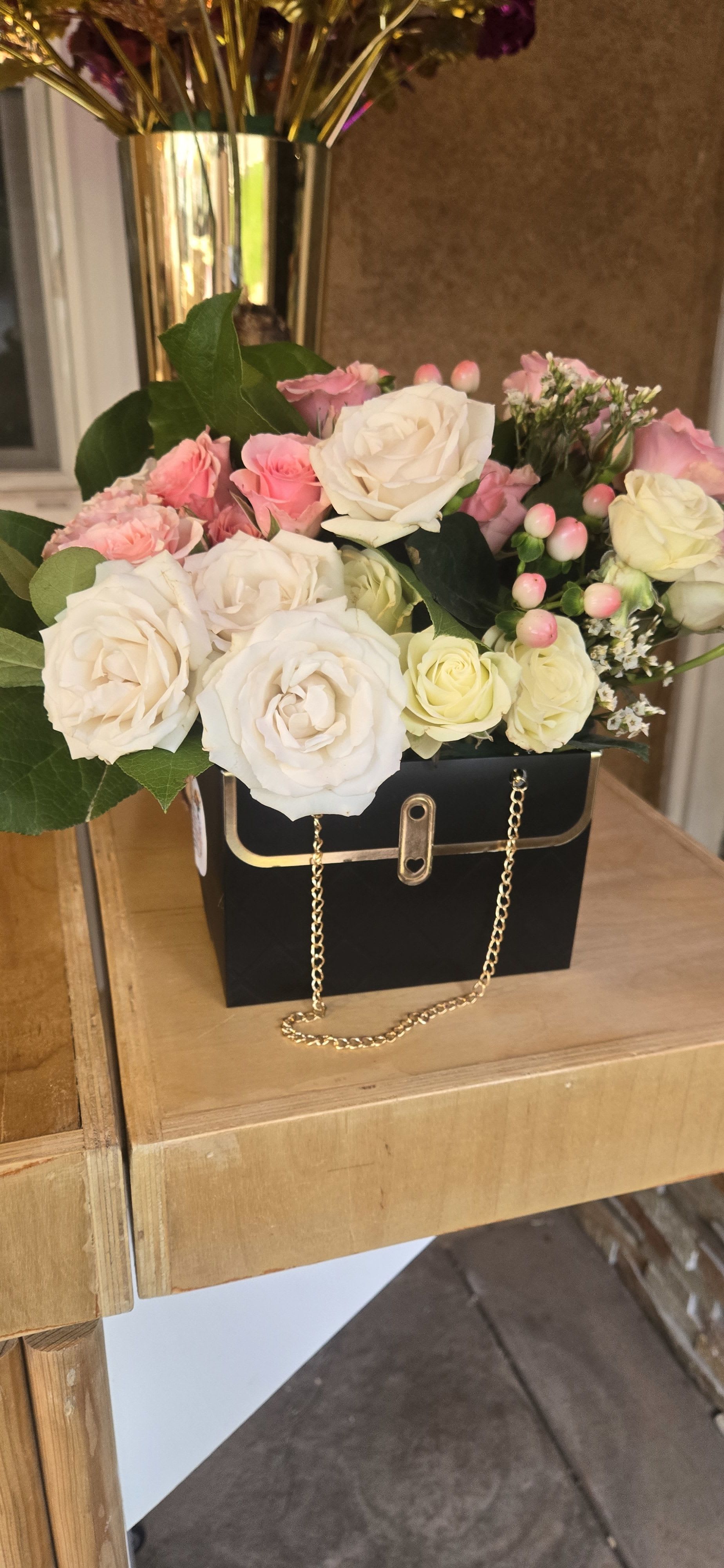 Pink and white roses arranged in a black handbag-style box