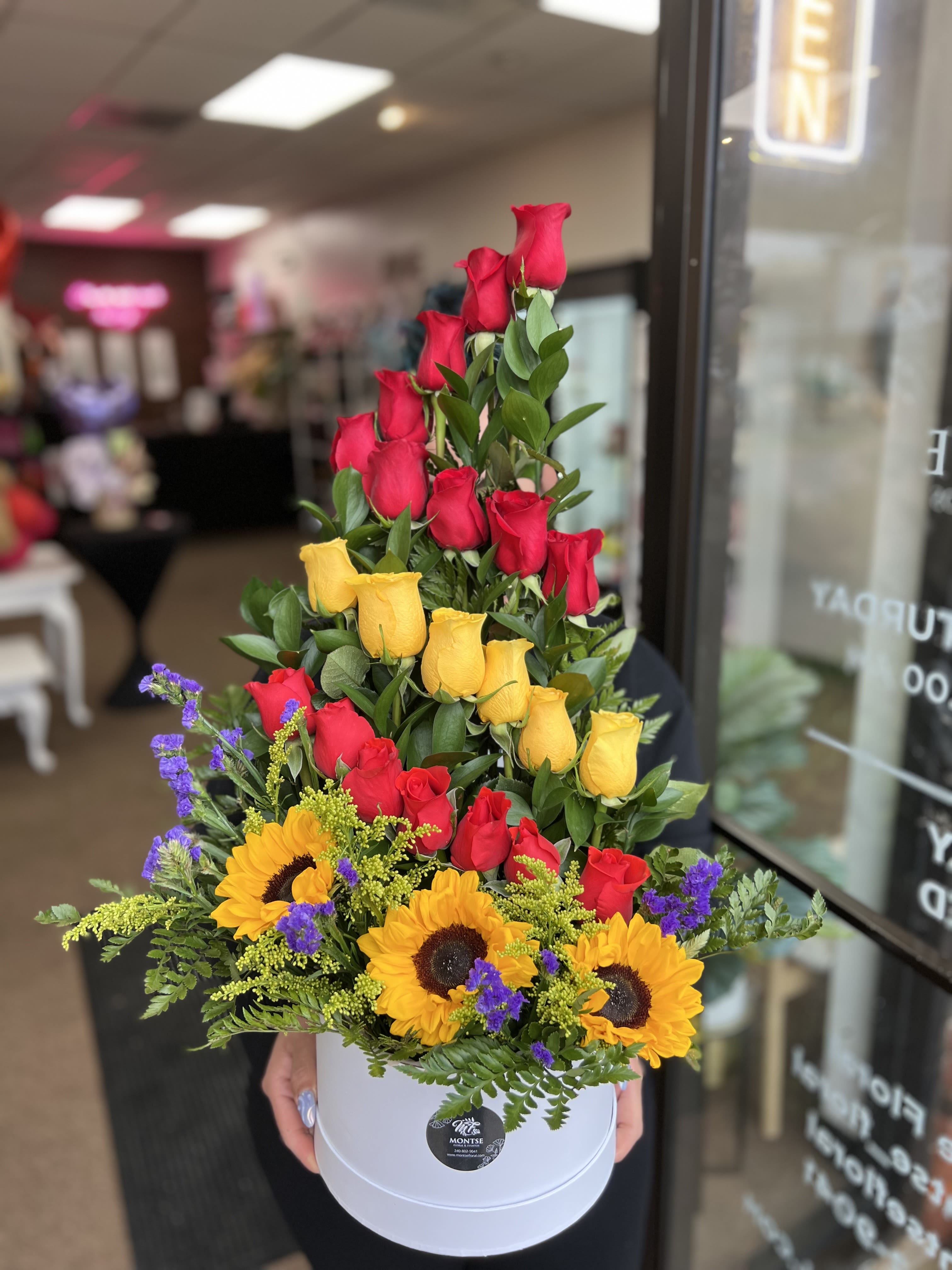 Tiered arrangement of red and yellow roses with sunflowers in a white box