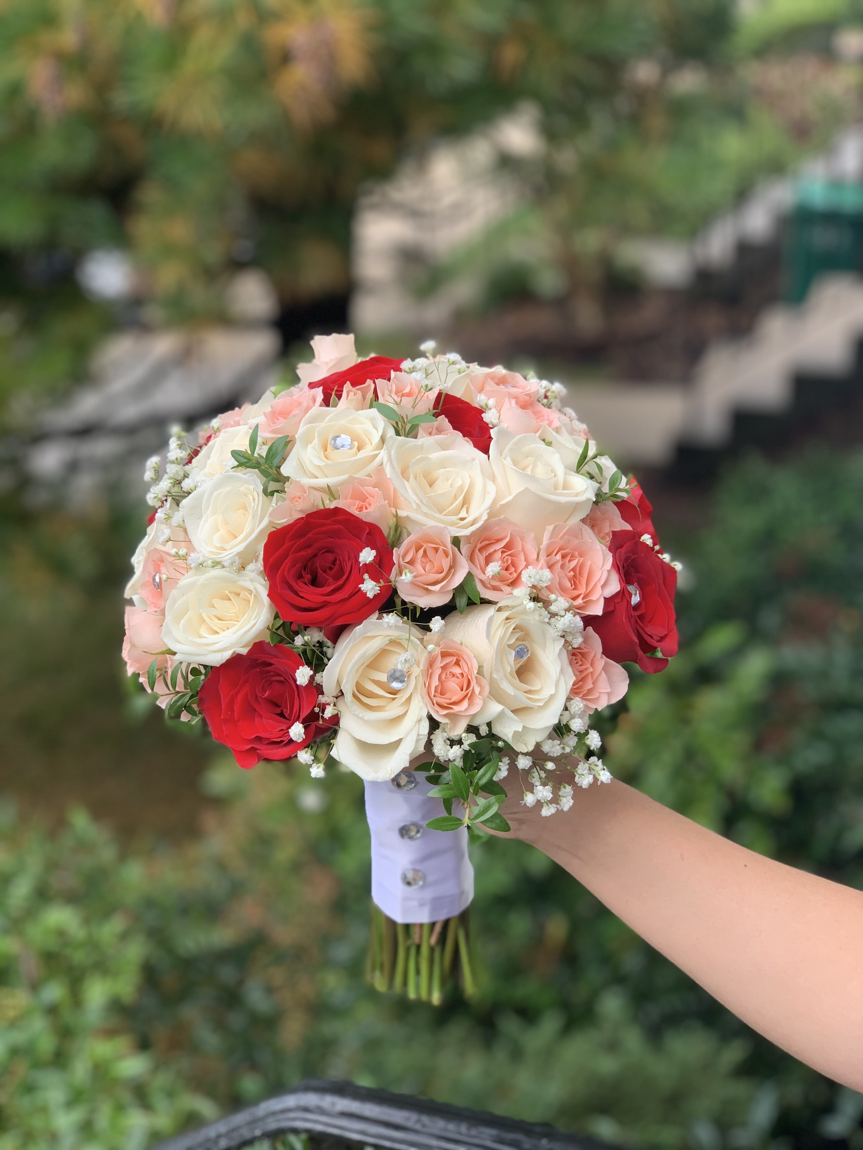 Handheld bouquet of red, white, and blush roses with baby's breath