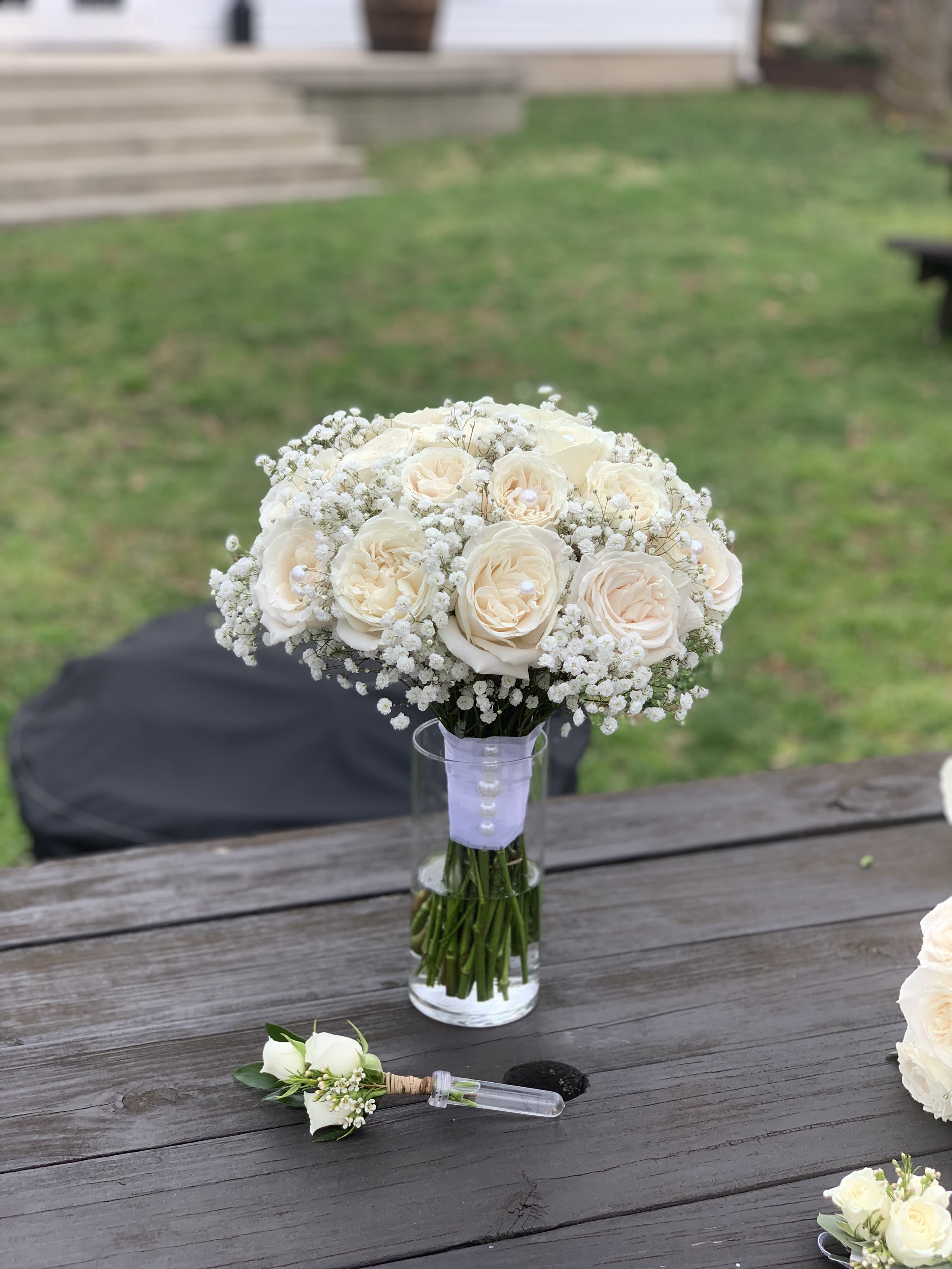 Cream rose bouquet in a glass vase with a matching boutonniere on a table