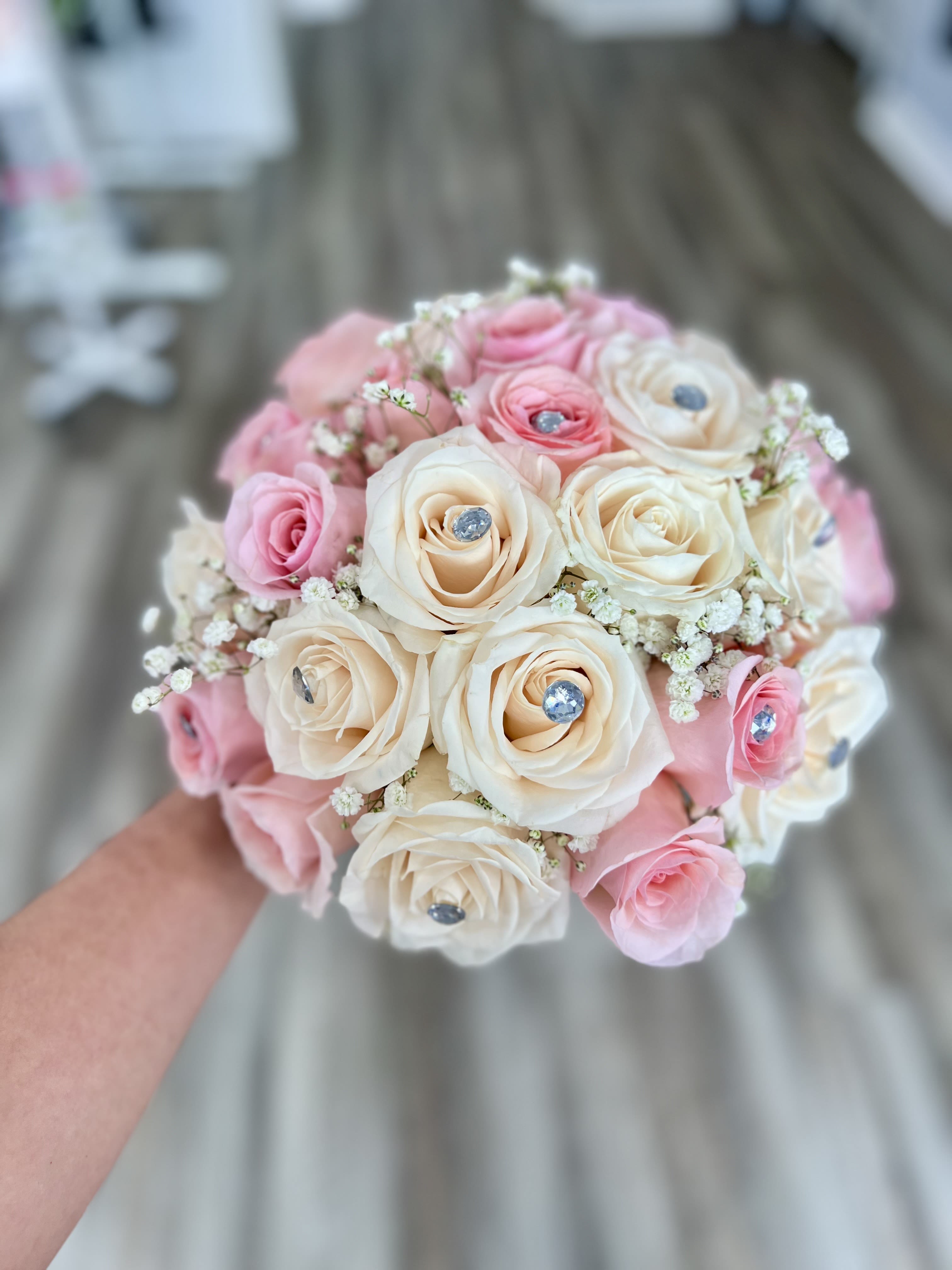 Handheld bouquet of pink and ivory roses with small white filler flowers