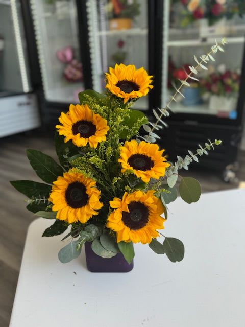 Sunflower arrangement in a purple vase with eucalyptus accents