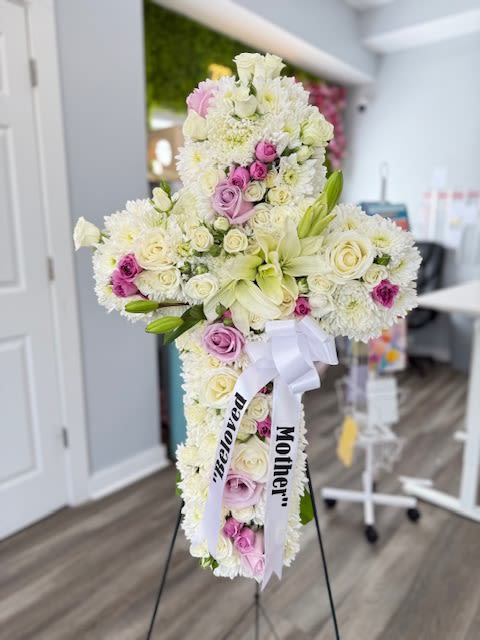 Cross-shaped floral tribute with white and pink flowers on a stand