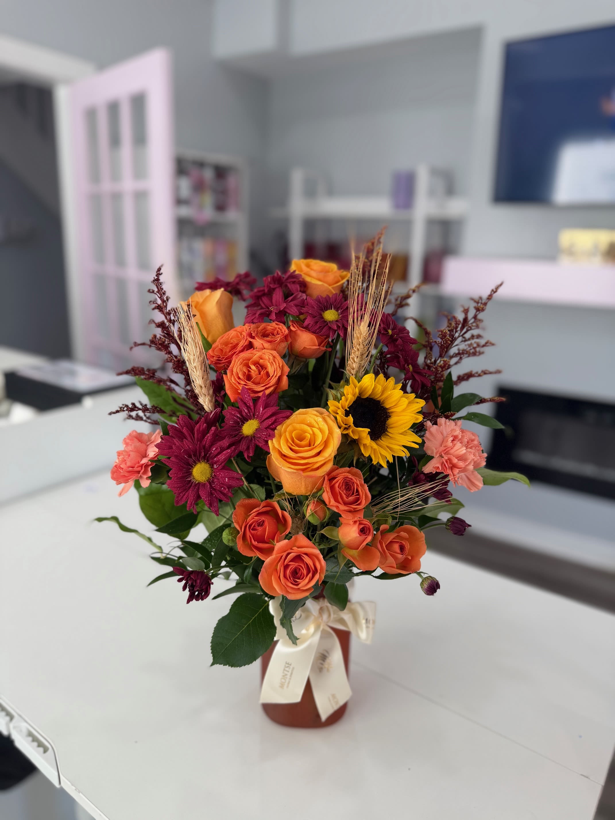 Bouquet of orange roses, burgundy daisies, and a sunflower in a vase