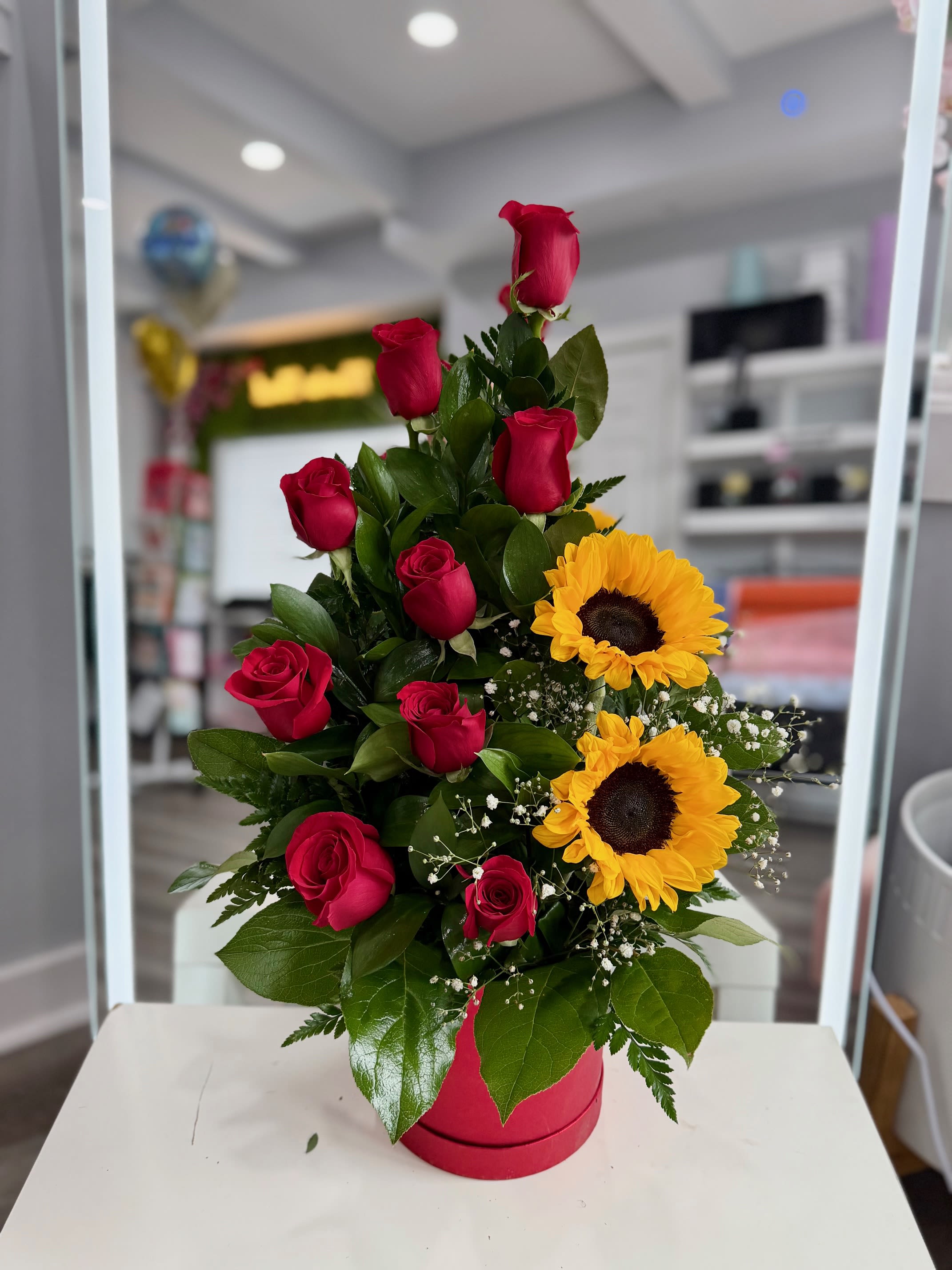 Red roses and sunflowers arranged in a pink box