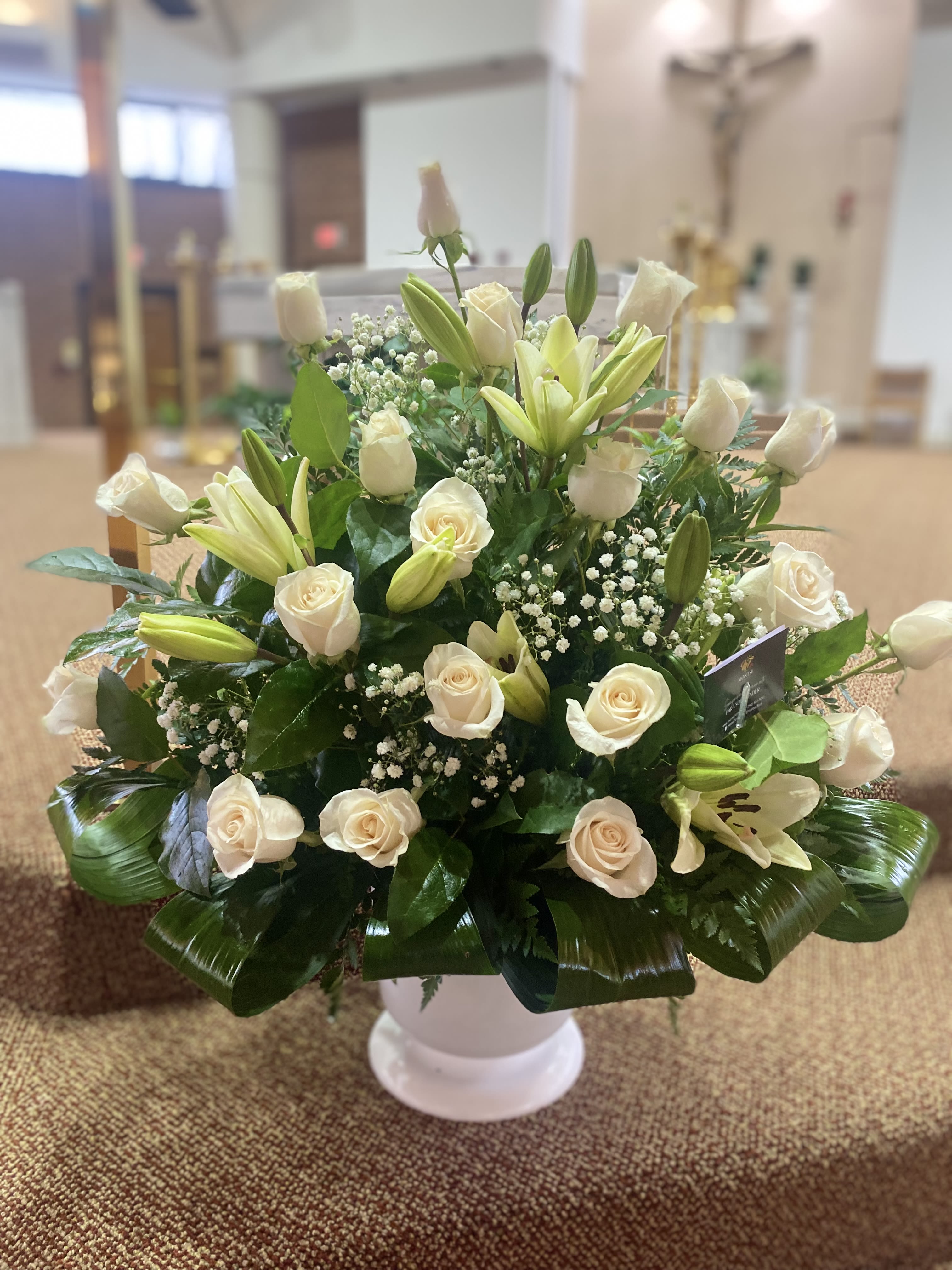 White roses and lilies arranged in a white pedestal vase