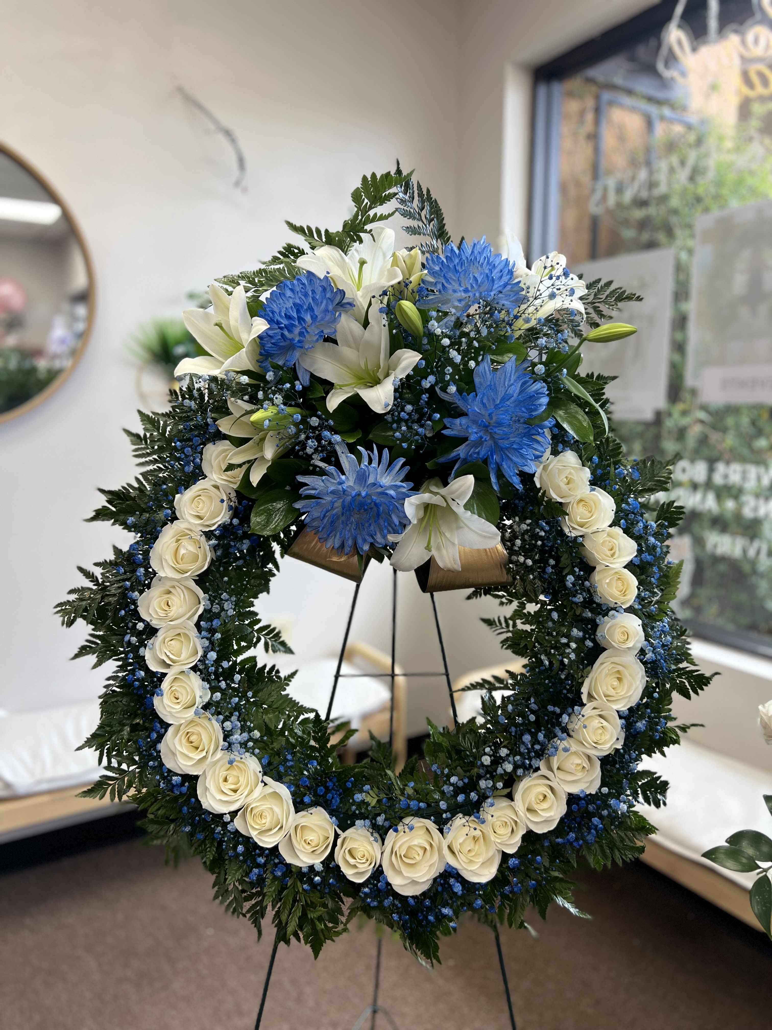 Large floral wreath with white roses, lilies, and blue flowers on a stand