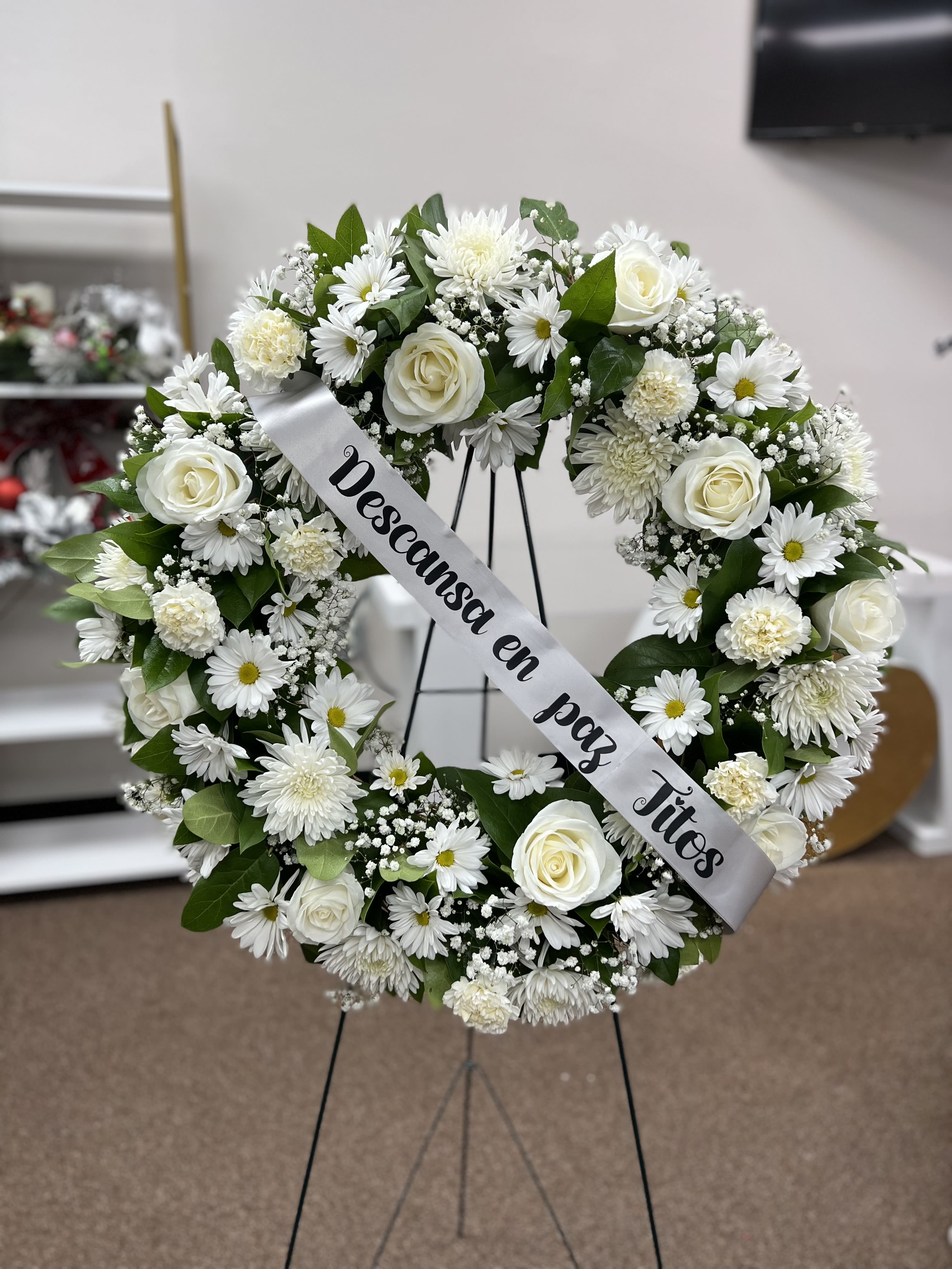 White floral funeral wreath on a stand with a memorial ribbon