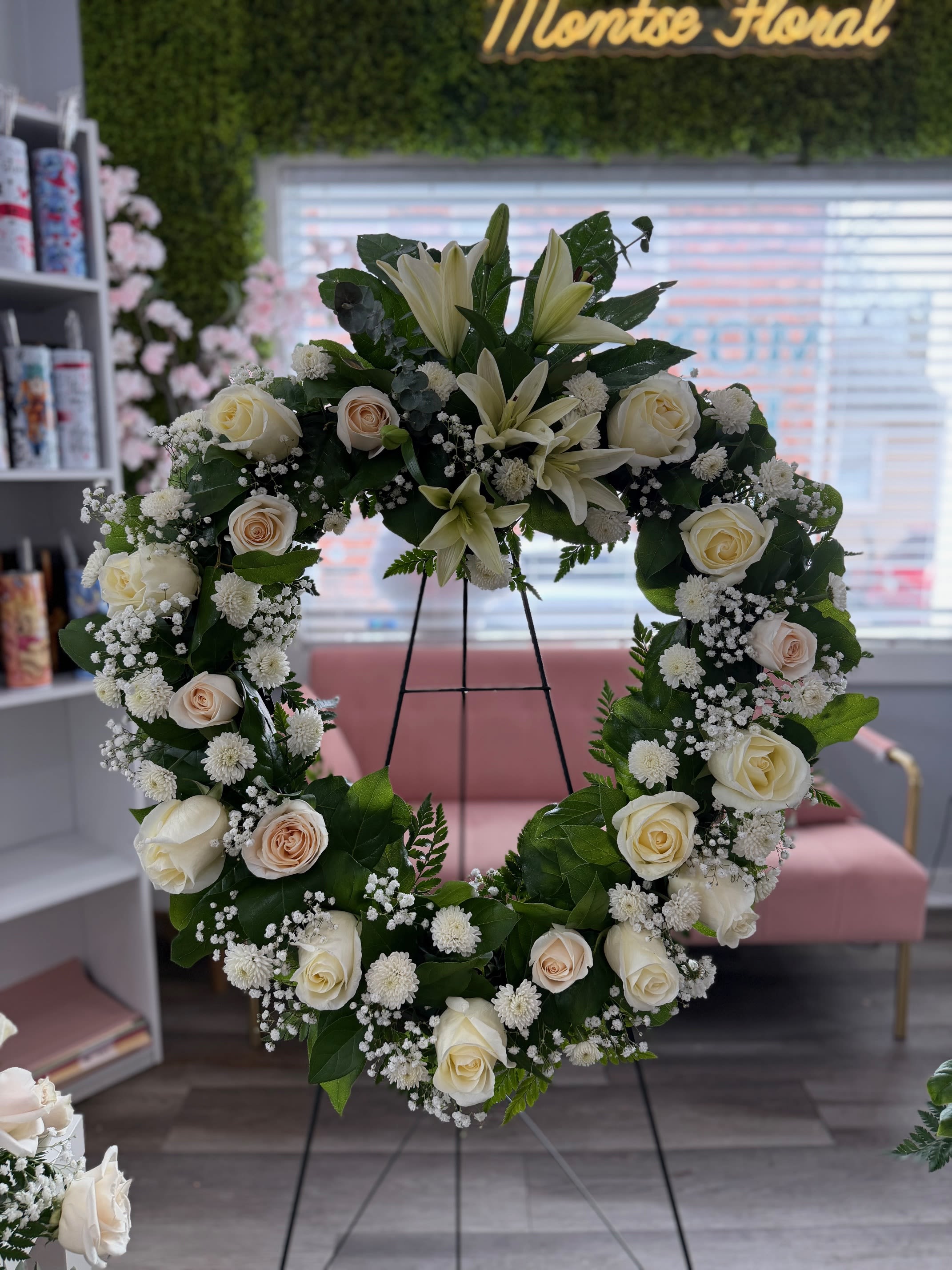 Standing wreath of white lilies, ivory roses, and small white blooms on a metal easel