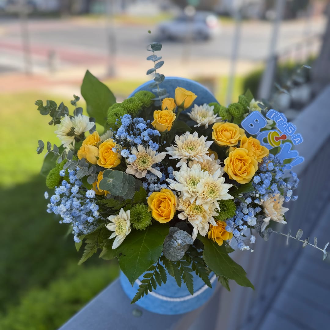 Yellow roses and white daisies in a blue vase with a baby-themed topper