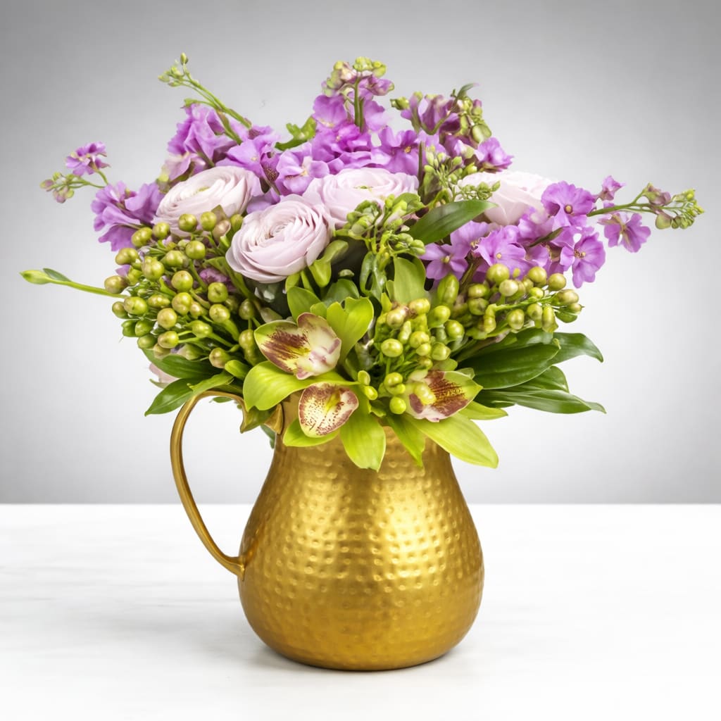 Rumors By BloomNation™ - Rumors By BloomNation™ is a bold and modern floral arrangement designed to stand out. This lush design features soft lavender blooms, premium pale pink ranunculus, vibrant green hypericum berries, cymbidium orchids, and fresh seasonal greenery arranged in a striking hammered gold container. The rich texture and layered design create depth, movement, and a refined finish.  Perfect for birthdays, celebrations, thank you gifts, or sending something unique, Rumors By BloomNation™ makes a strong impression in any home or office. Designed by expert florists using premium fresh flowers, this arrangement delivers both elegance and impact.  Available for same-day flower delivery in Houston, this luxury floral design is ideal when you need a trusted Houston florist to deliver something unforgettable. Each arrangement is hand-crafted to ensure freshness, balance, and presentation.  Order Rumors By BloomNation™ today for reliable same-day flower delivery in Houston from a top-rated local florist.