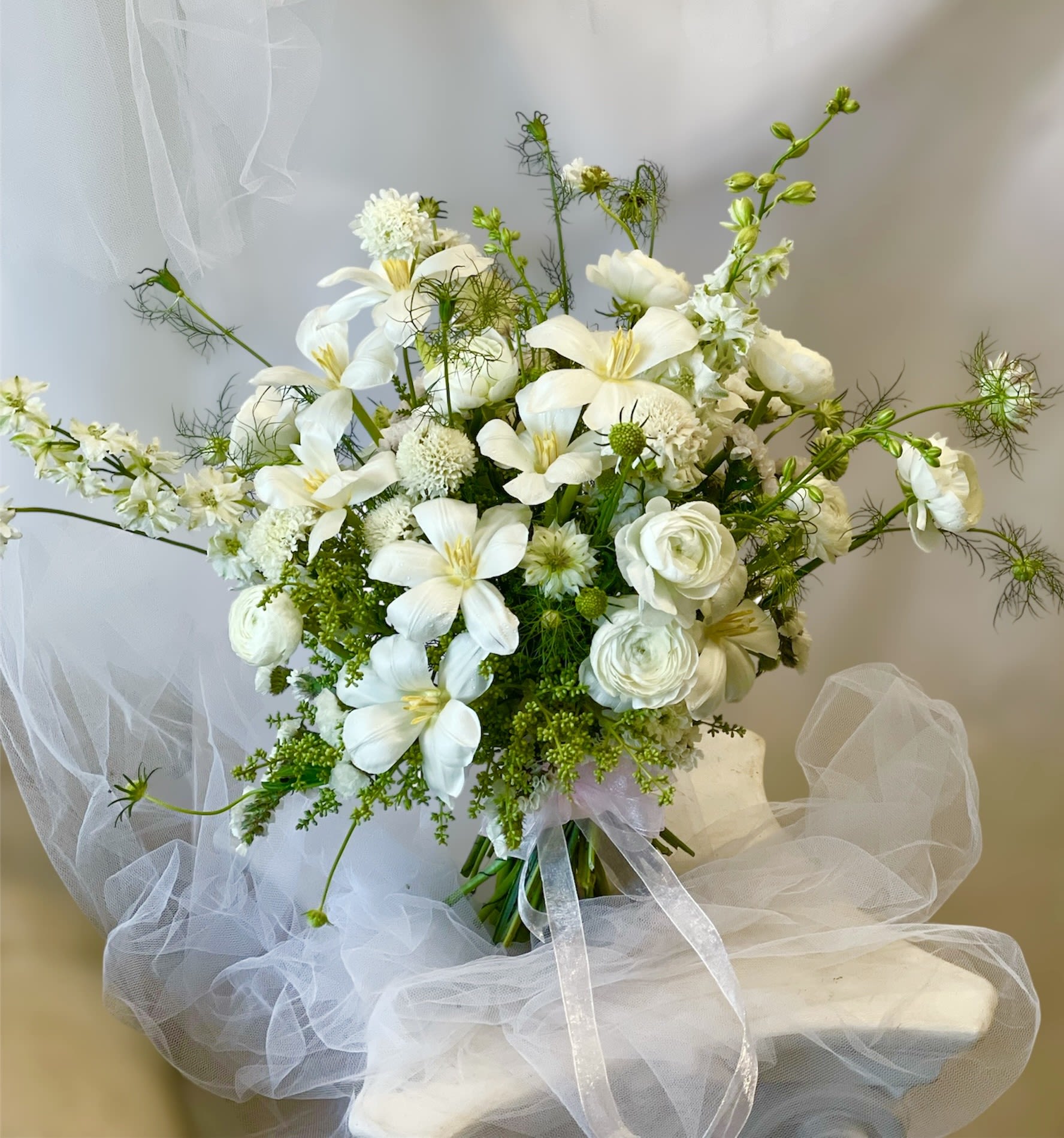 White floral bouquet with lilies and ranunculus tied with a sheer ribbon