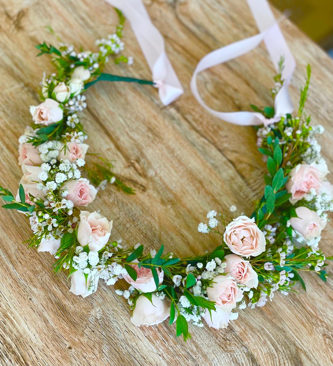 Floral crown with pale pink roses and white filler flowers on a wooden surface