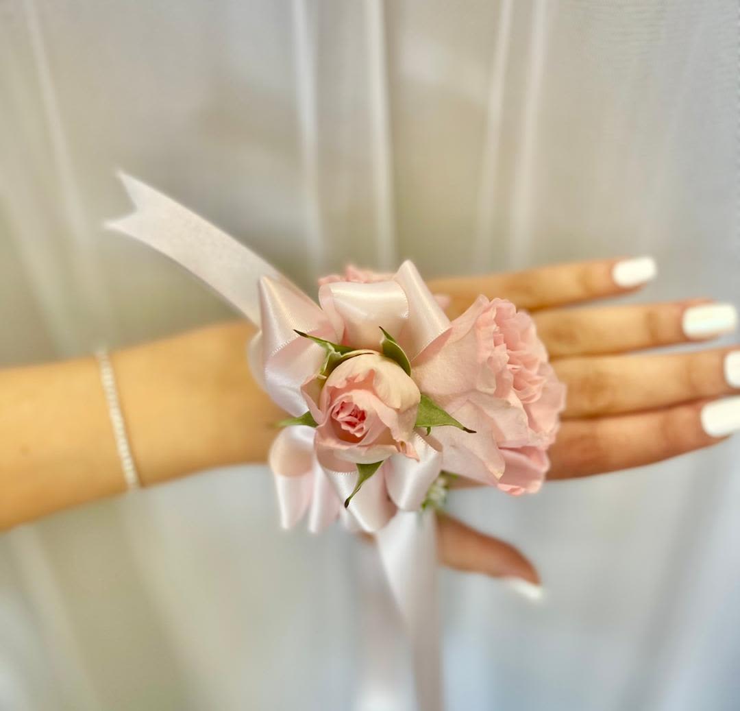 Pink floral wrist corsage with satin ribbon on a hand
