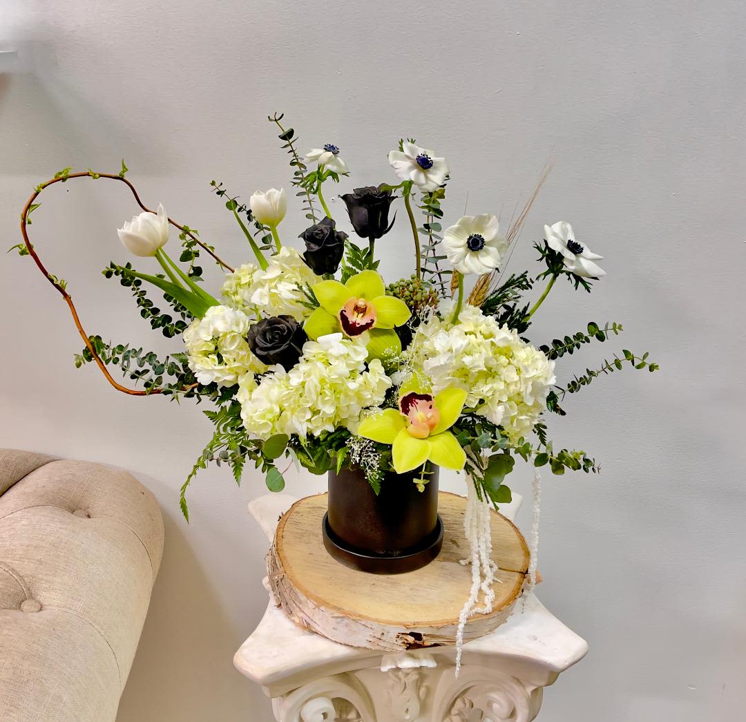White and black floral arrangement with yellow orchids in a dark vase