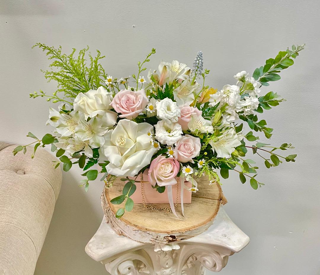 Pink and white floral arrangement in a pink box on a wood slice stand