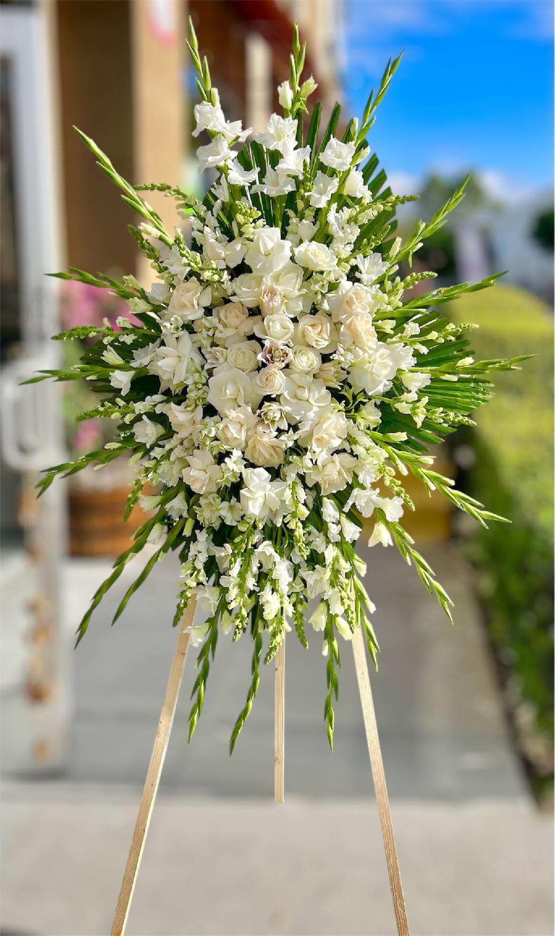 White floral standing spray on an easel with long green accents