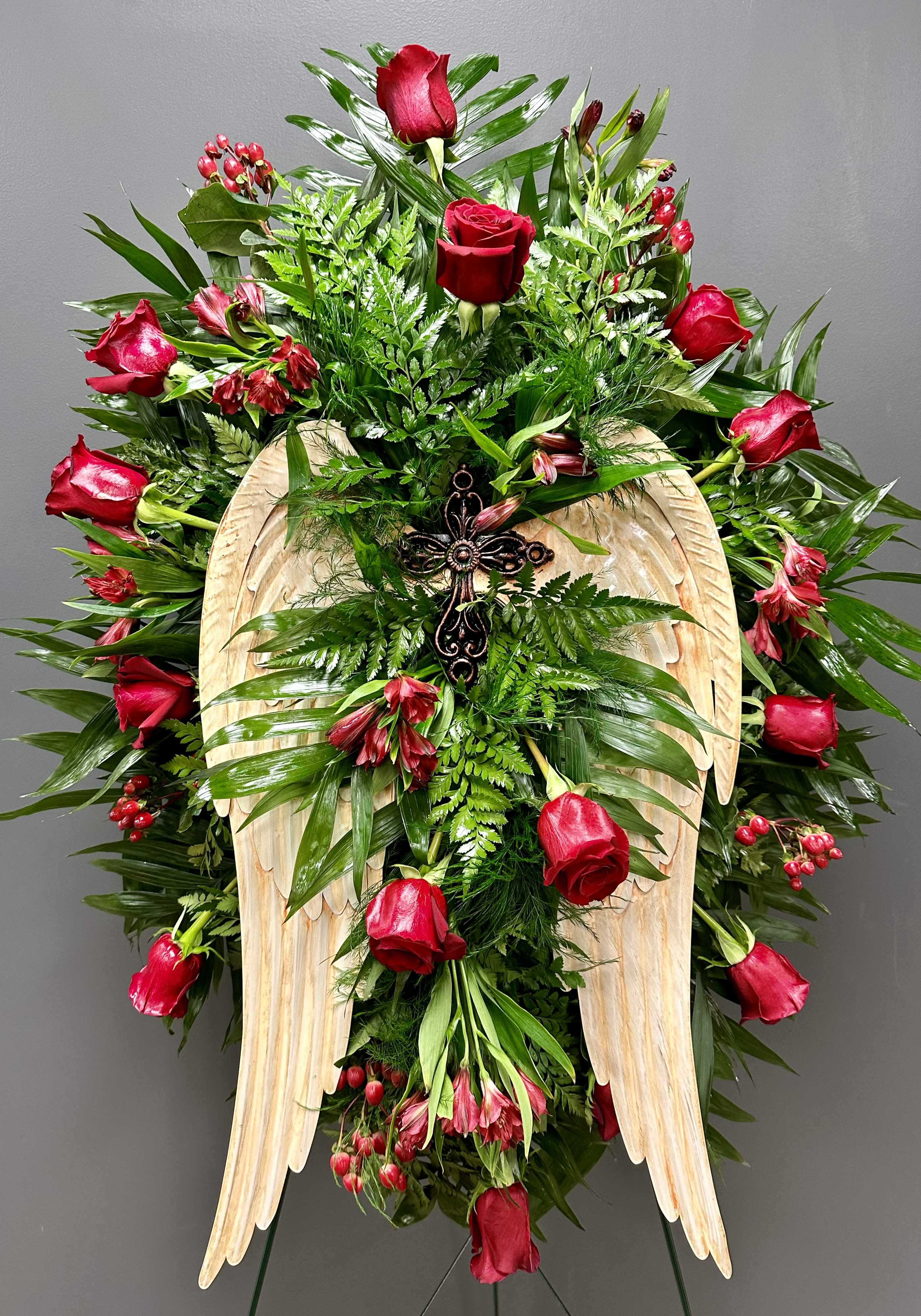 Standing floral spray with red roses and a wooden angel-wing cross