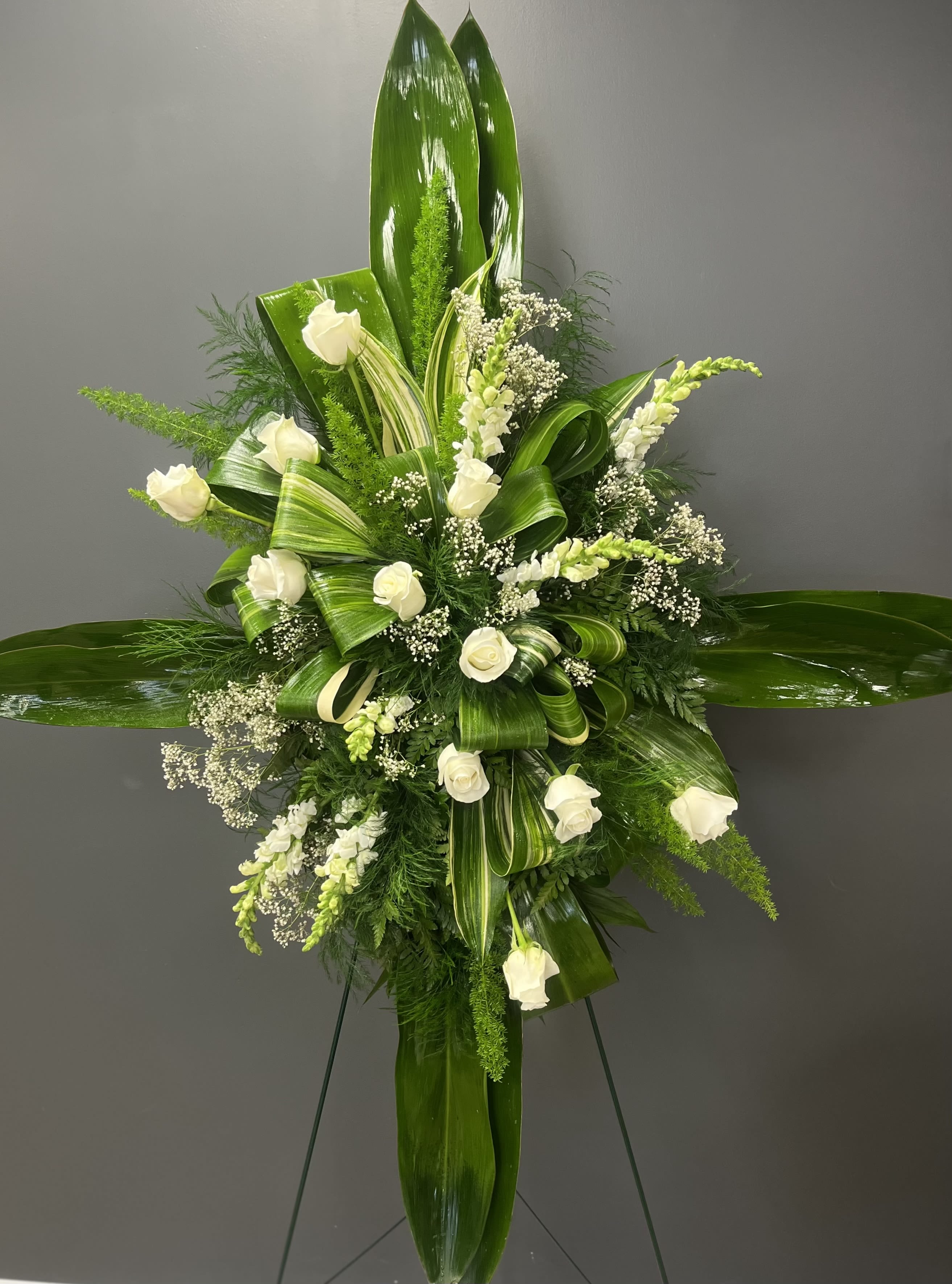 White roses and small white blooms arranged with glossy green leaves on a standing easel.