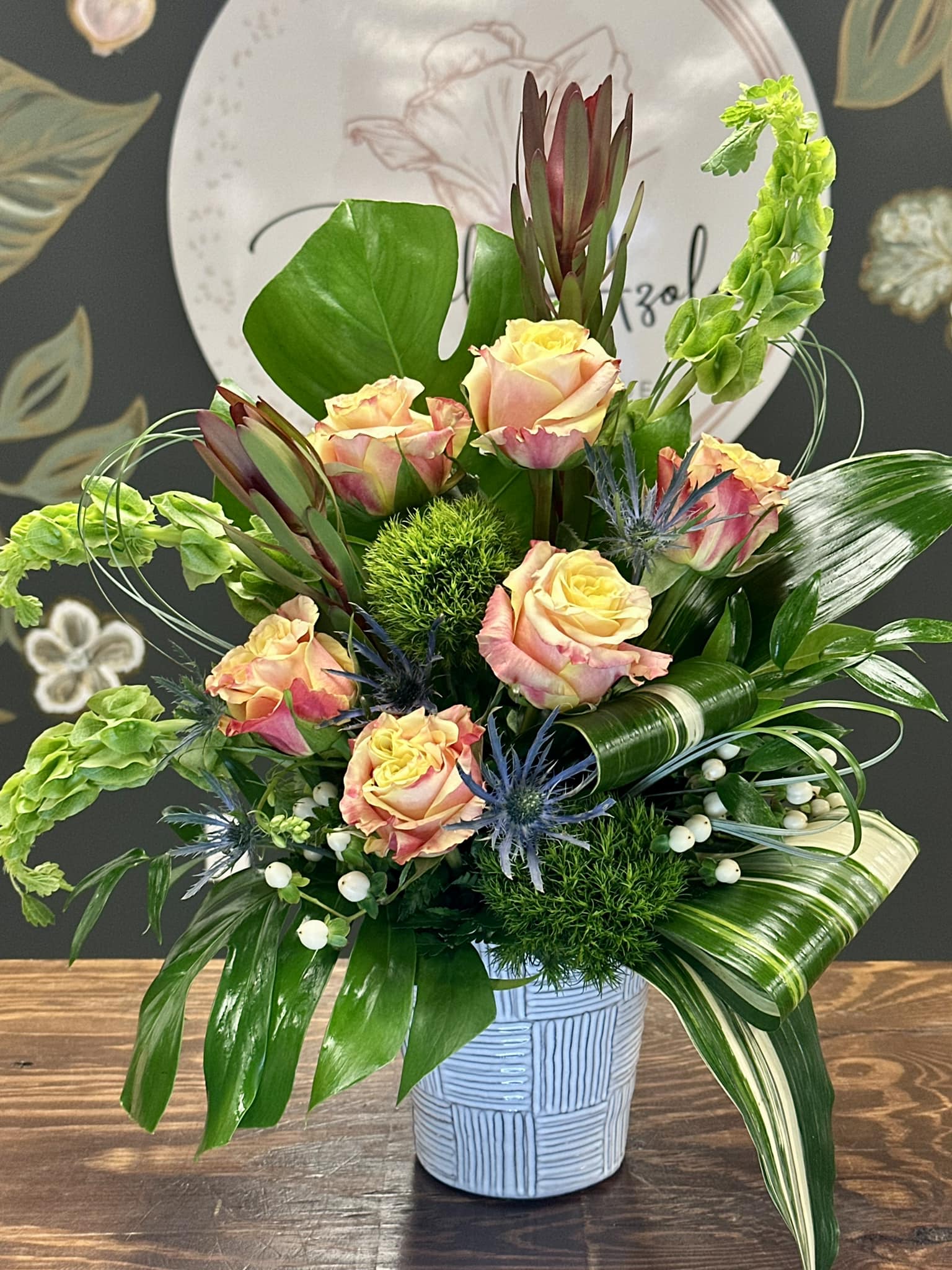 Mixed bouquet of peach roses and green foliage in a blue vase