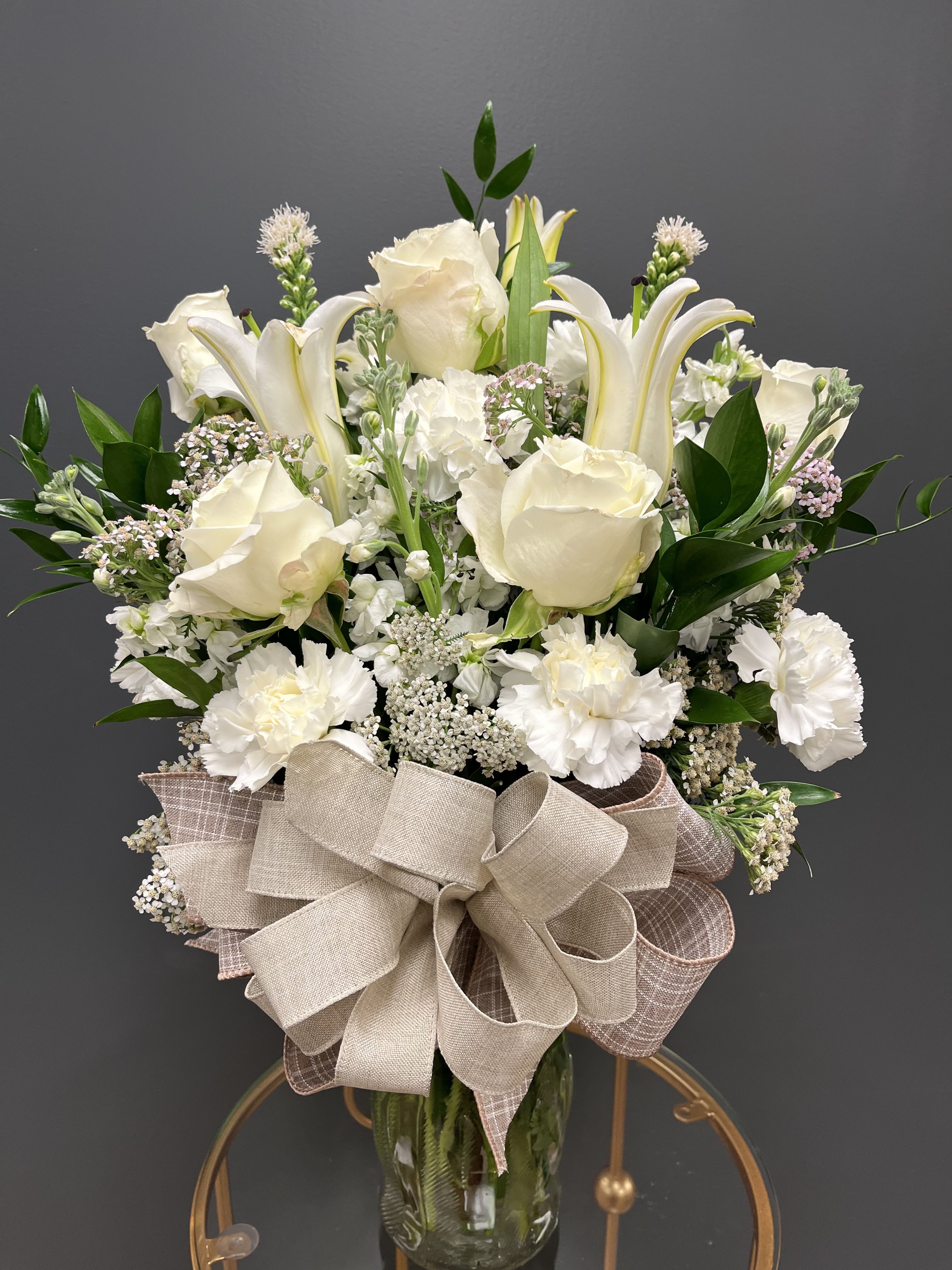 White roses and lilies in a glass vase with a large beige bow