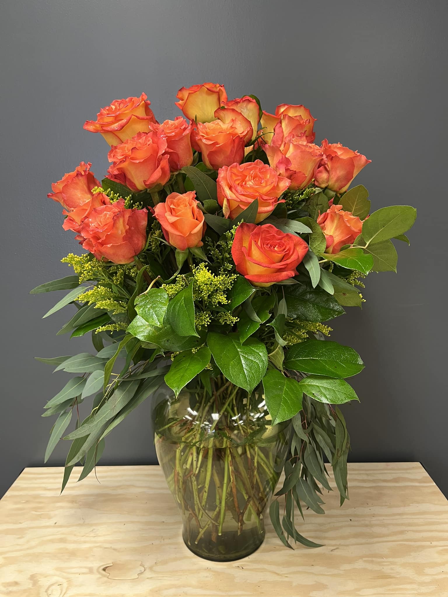Orange roses arranged in a glass vase with greenery