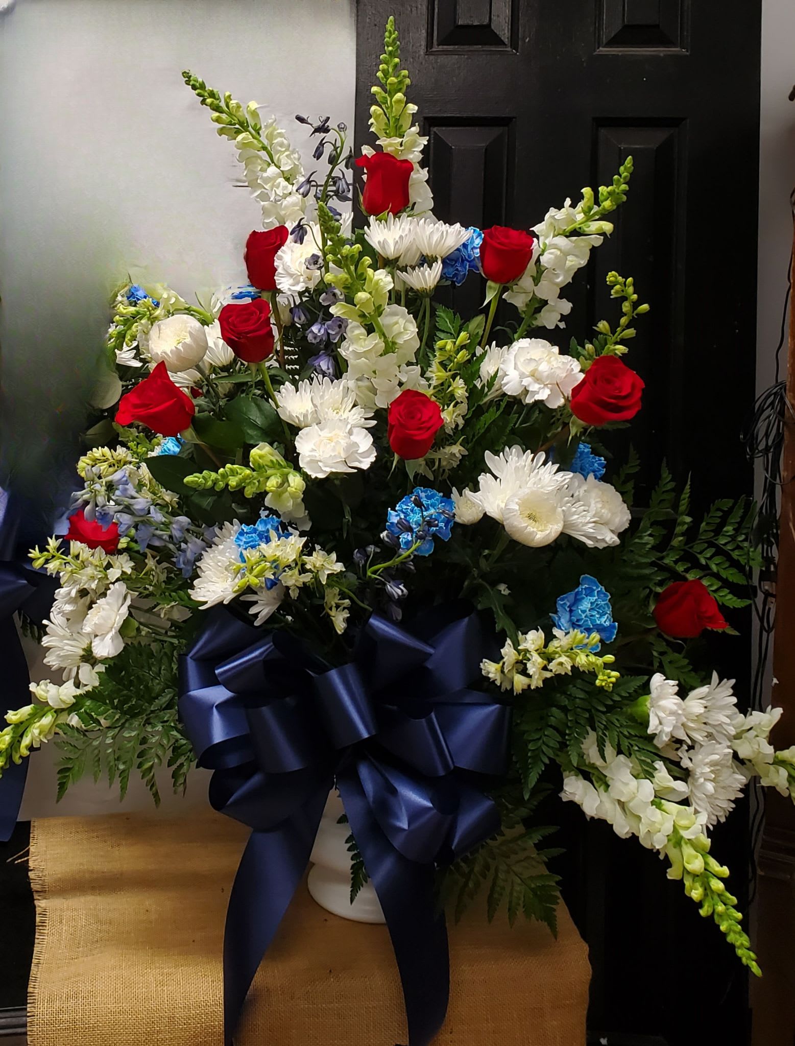 Large floral arrangement with red roses, white blooms, and blue accents in a white vase