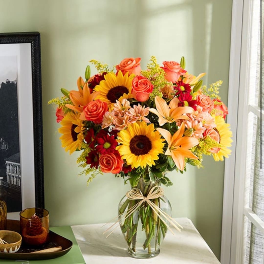 Bouquet of sunflowers, roses, lilies, and daisies in a glass vase