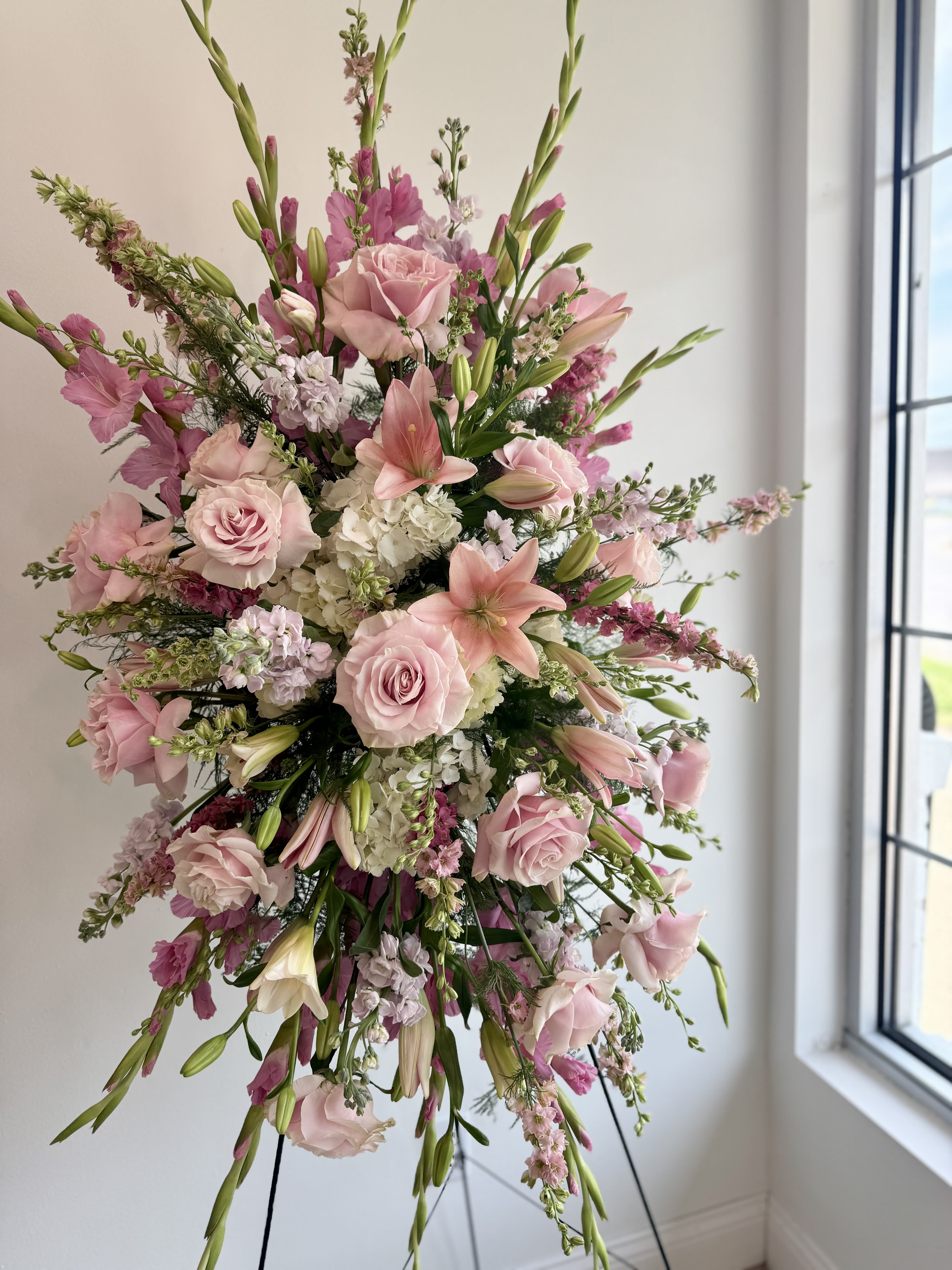 COMPASSION PINK STANDING SPRAY - A graceful pink standing spray featuring an array of soft, delicate blooms, offering a heartfelt tribute and a symbol of love and remembrance.
