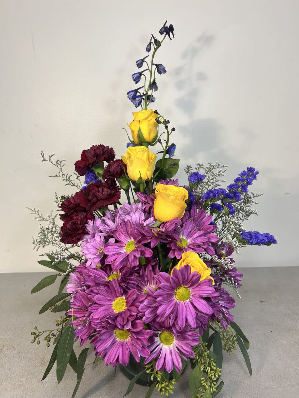 Tall bouquet of purple daisies, yellow roses, and dark red carnations