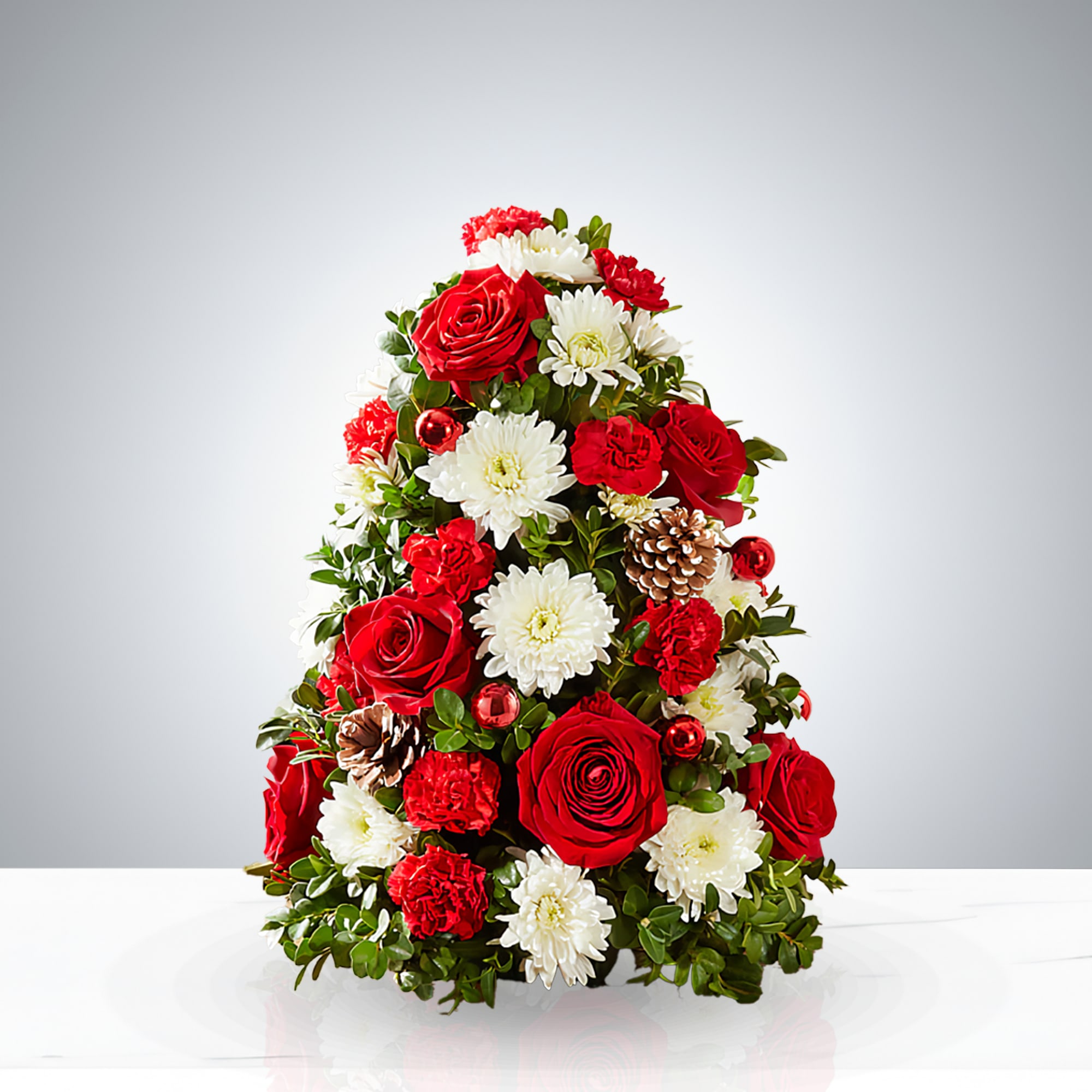 Eternal Christmas - Celebrate the season with Eternal Christmas, a handcrafted floral arrangement shaped like a Christmas tree. Featuring vibrant red roses, snowy white chrysanthemums, lush carnations, pinecones, and festive ornaments, this conical design brings timeless holiday charm to any space. Perfect for centerpieces, gifts, or seasonal décor, it blends natural elegance with joyful tradition.