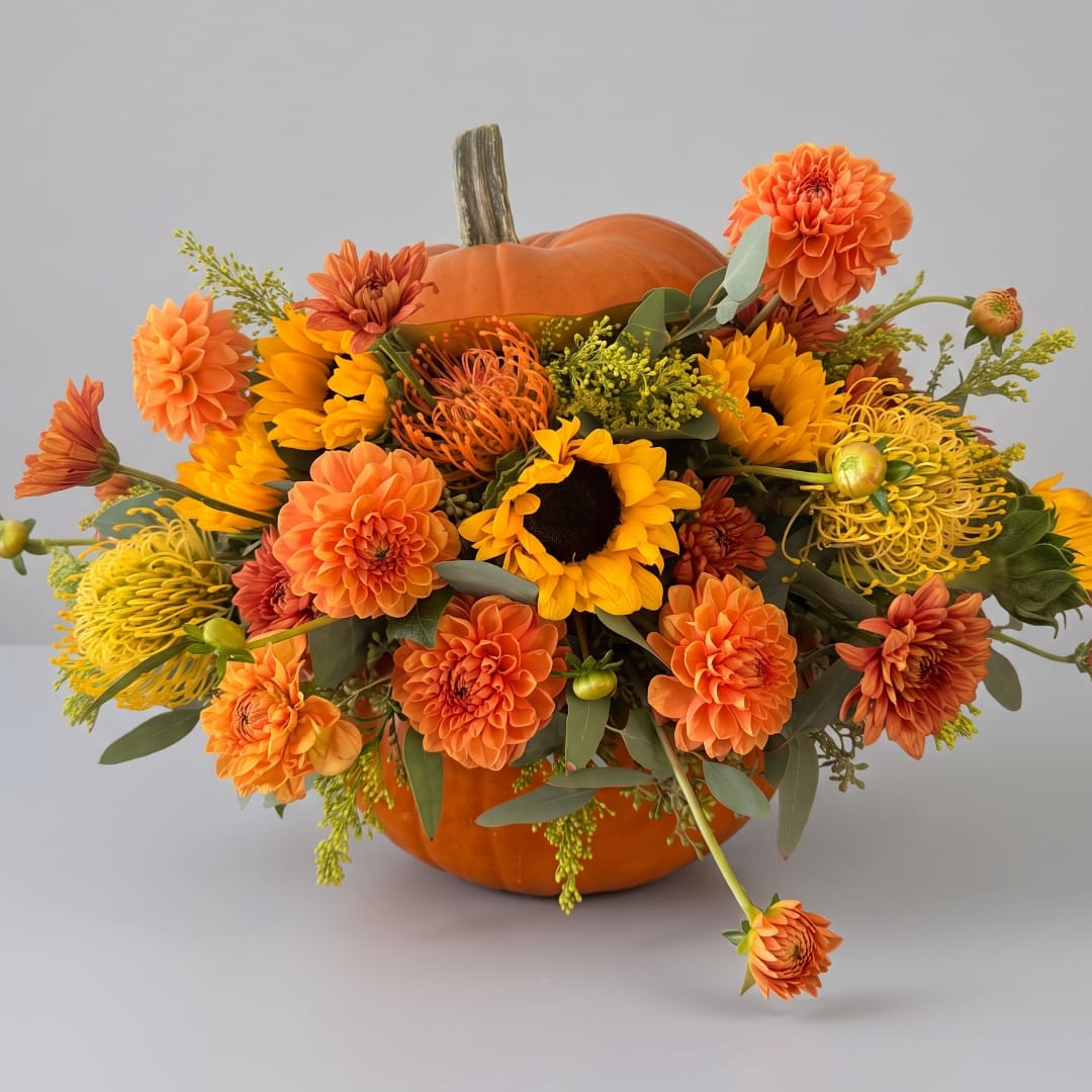 Orange floral arrangement in a pumpkin container with sunflowers and dahlias