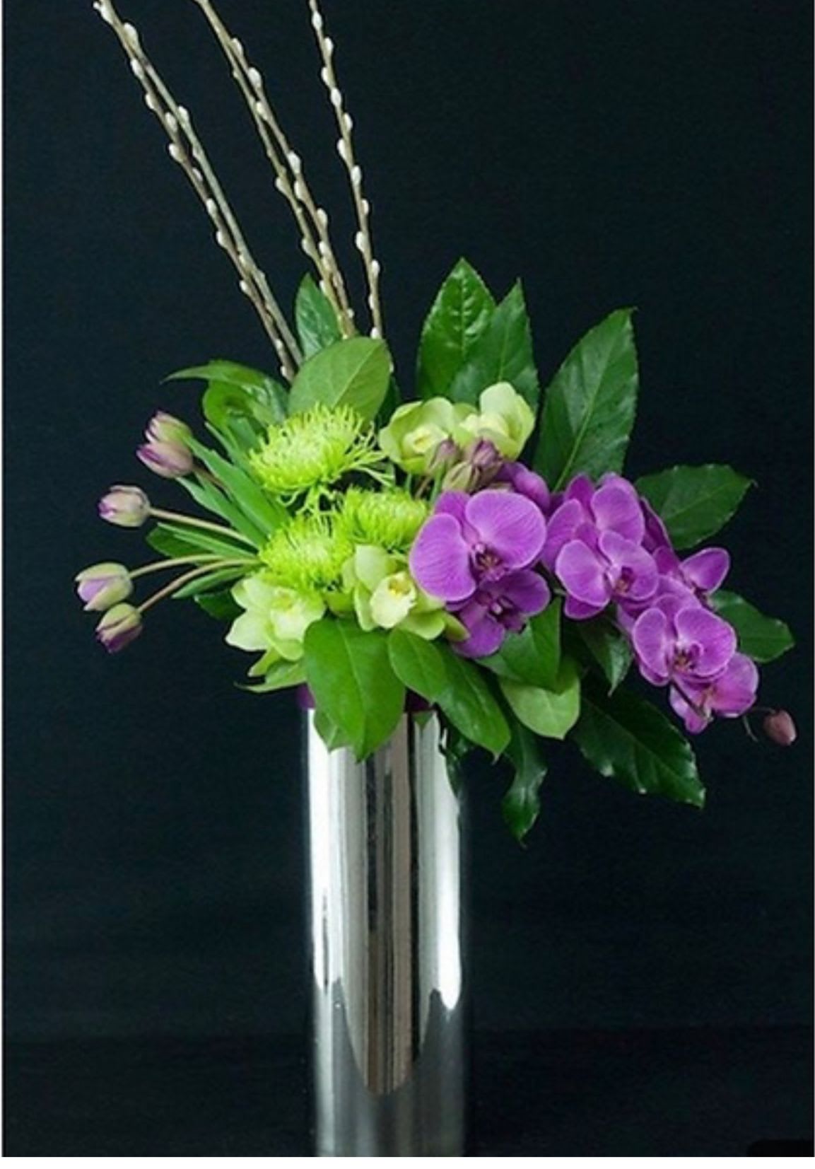 Purple orchids and green flowers in a tall silver vase