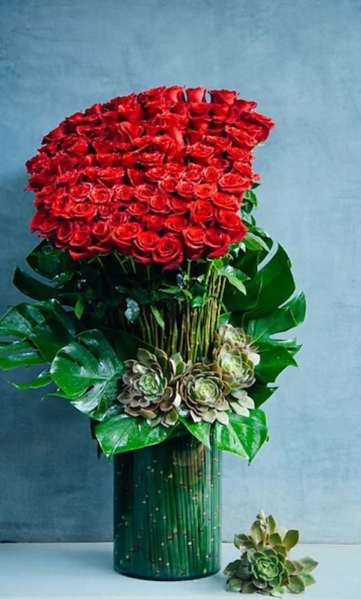 Large red rose arrangement in a tall green vase with succulents