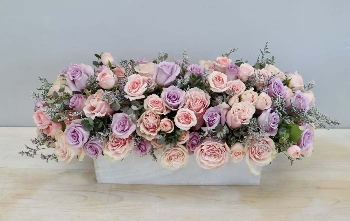 Low rectangular arrangement of pink and lavender roses in a white container