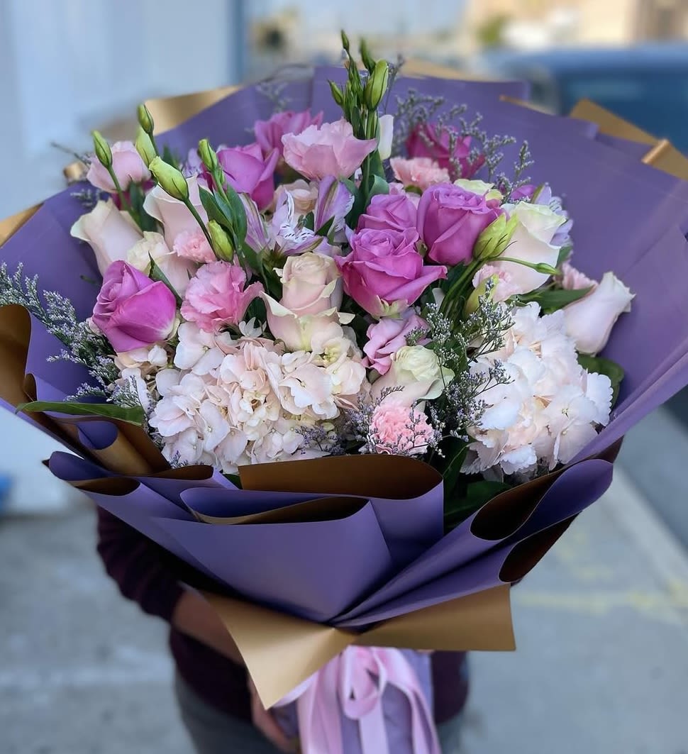 Bouquet of pink and white roses with pale hydrangeas wrapped in purple paper
