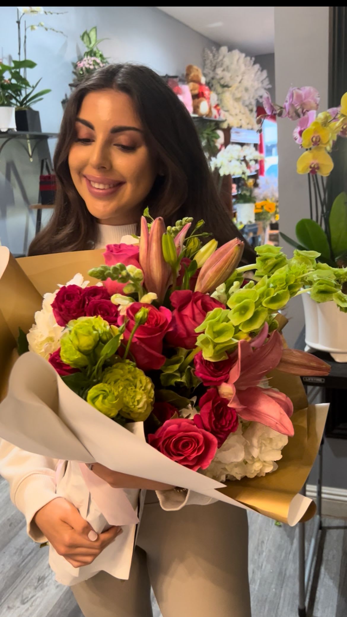 Woman holding a colorful bouquet of roses, lilies, and green blooms