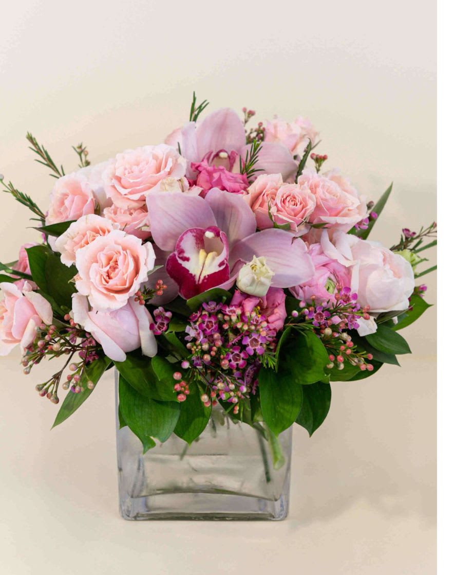 Pink roses and orchids arranged in a clear square vase